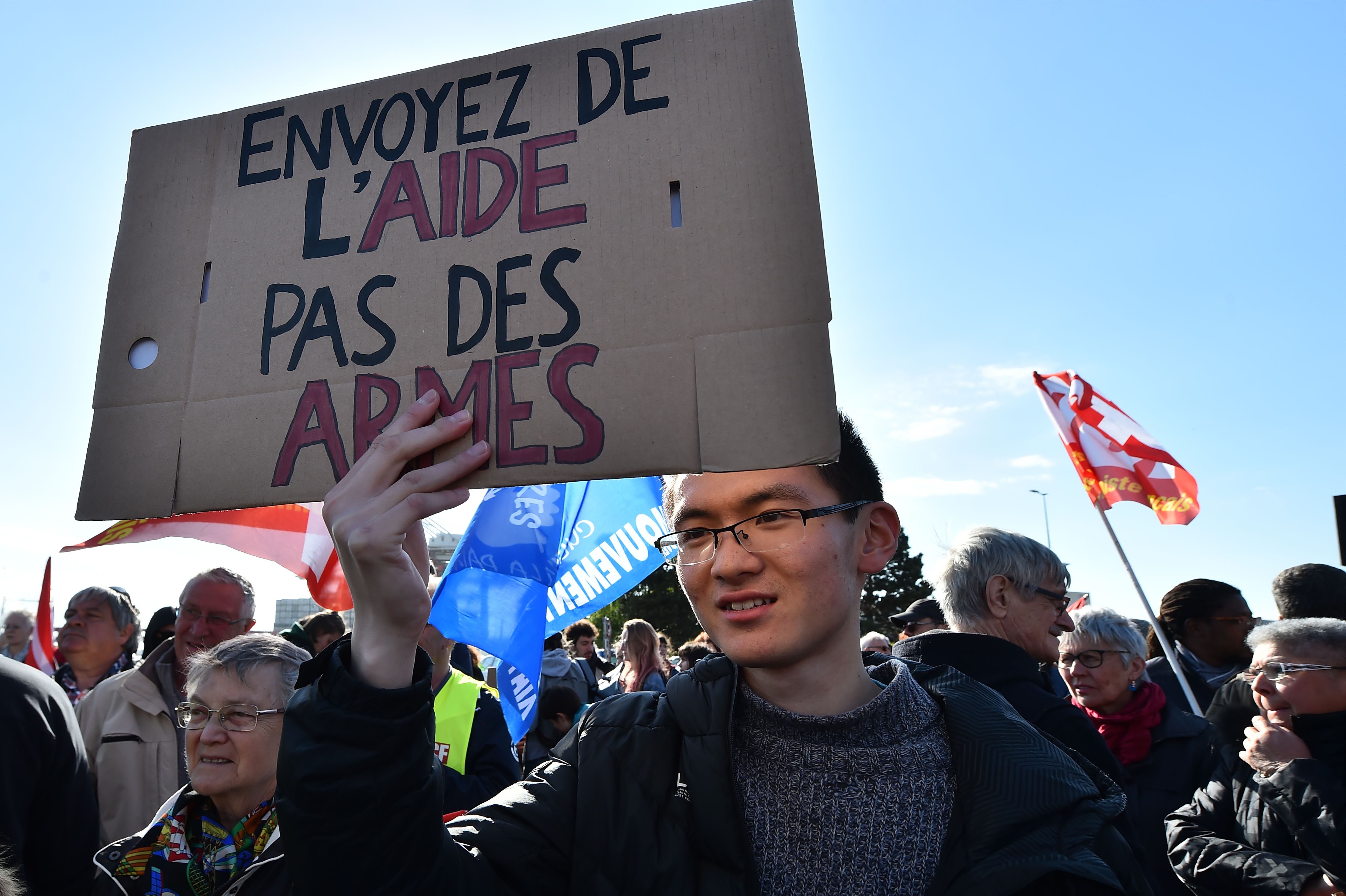 Un manifestant tient une pancarte sur laquelle on peut lire "Envoyez de l'aide, pas des armes"