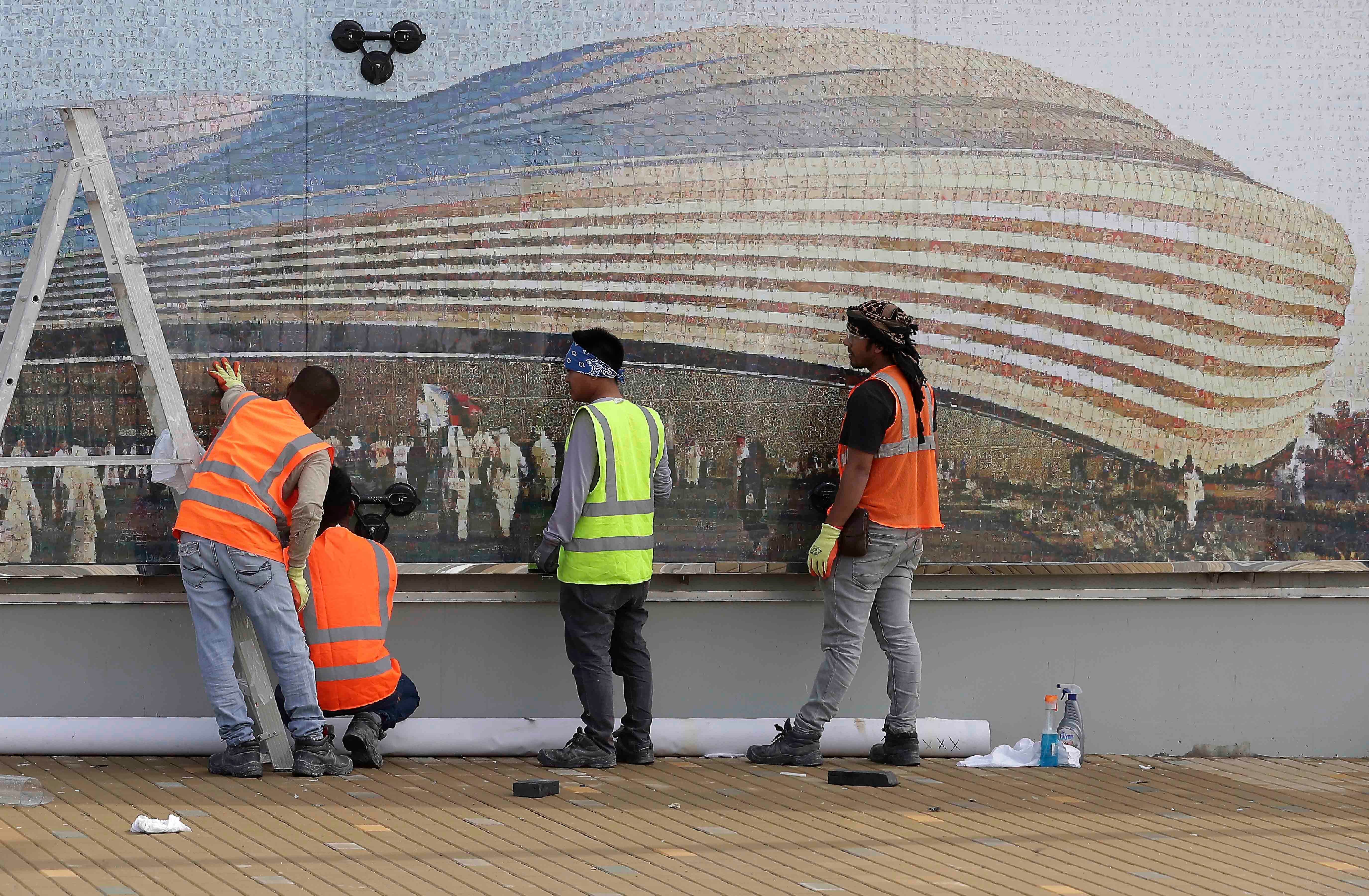 Workers in front of a mural of a stadium 