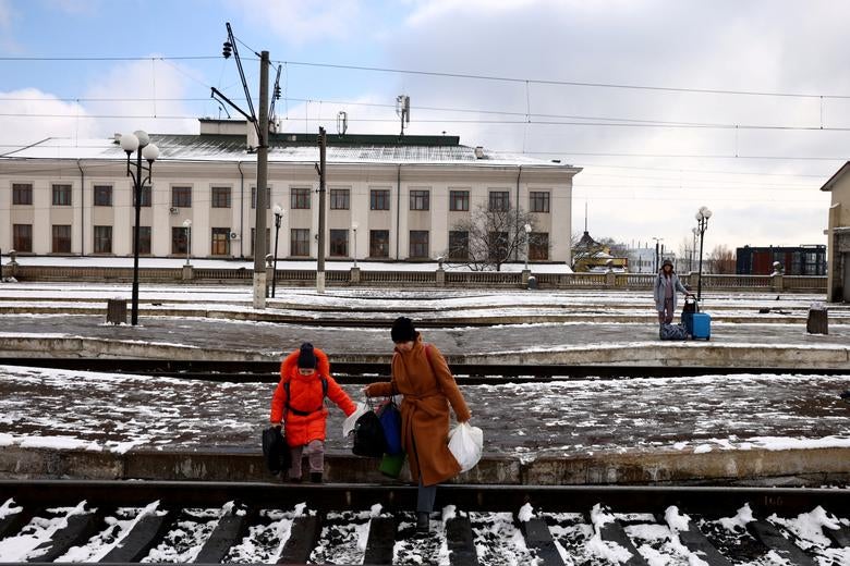 People fleeing Russia's invasion of Ukraine, cross train tracks to get to a train leaving for Poland, at the train station in Lviv