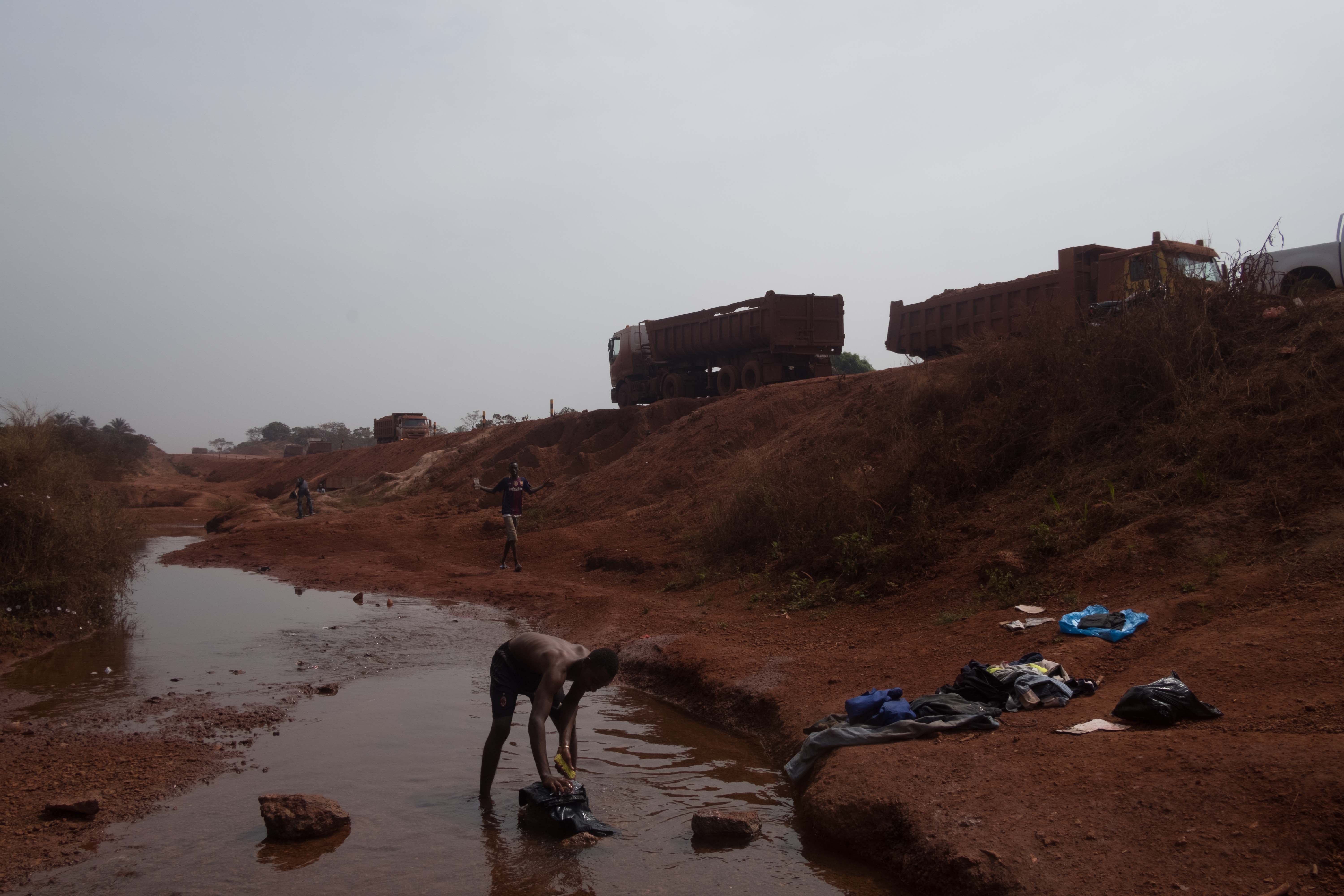 Un homme lave ses vêtements au bord d’une route utilisée par un consortium minier actif dans l’exploitation de la bauxite en Guinée. Les membres de communautés locales ont déclaré que la construction des routes minières a obstrué des rivières et ruisseaux, détournant leur cours et asséchant les puits locaux. 