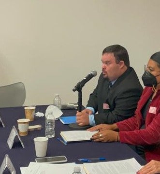 A man seated at a table speaks into a microphone