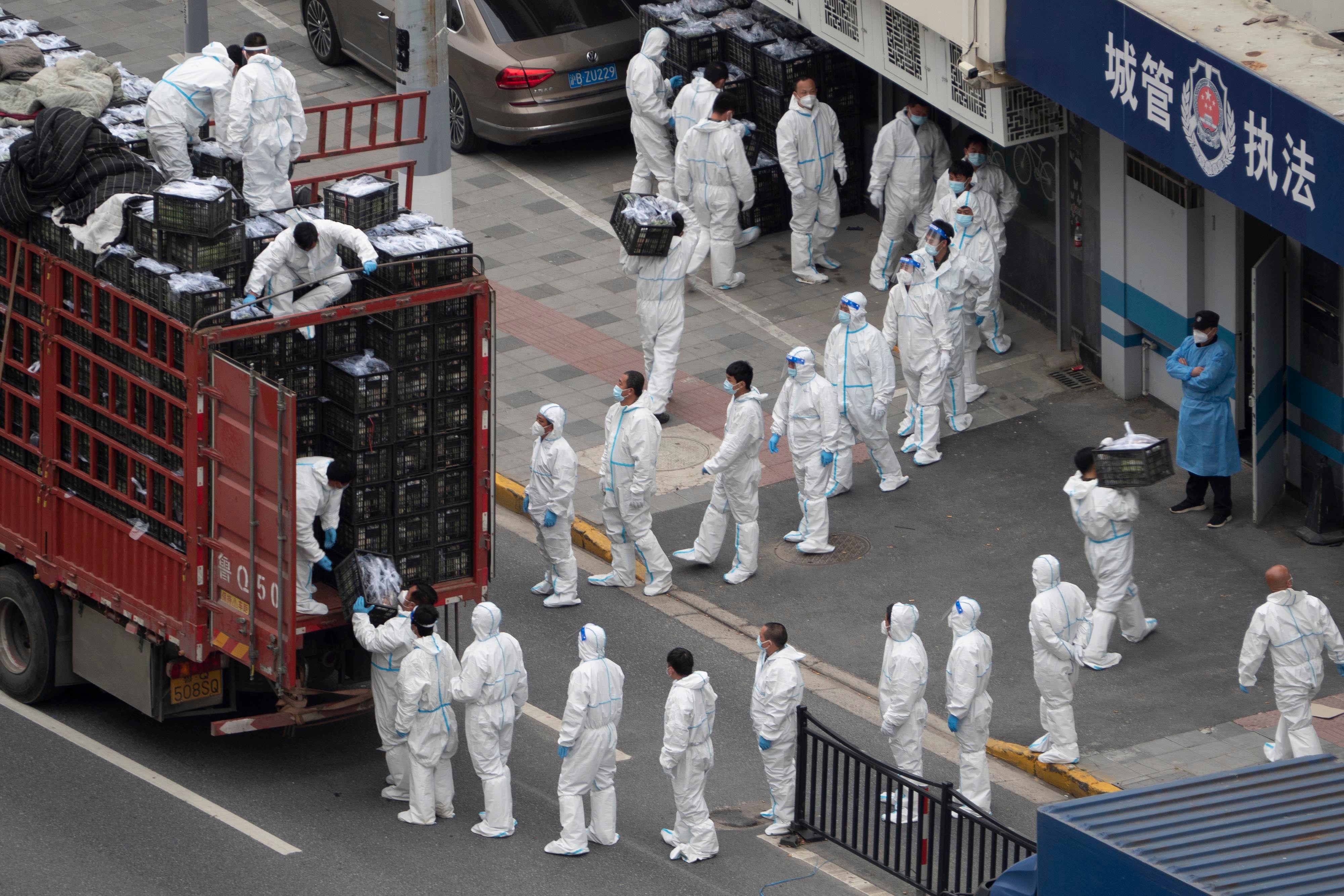 新冠疫情封城期间，穿着白色防疫服的人员从卡车上卸下物资，准备分发给市民，中国上海，2022年4月5日。