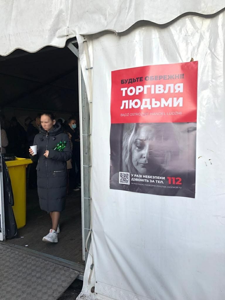Plakat na namiocie pomocy humanitarnej na warszawskim Dworcu Centralnym ostrzegający uchodźców przed handlem ludźmi i wzywający do wykonania telefonu pod numer alarmowy 112 w razie obaw, 26 marca 2022 r.
