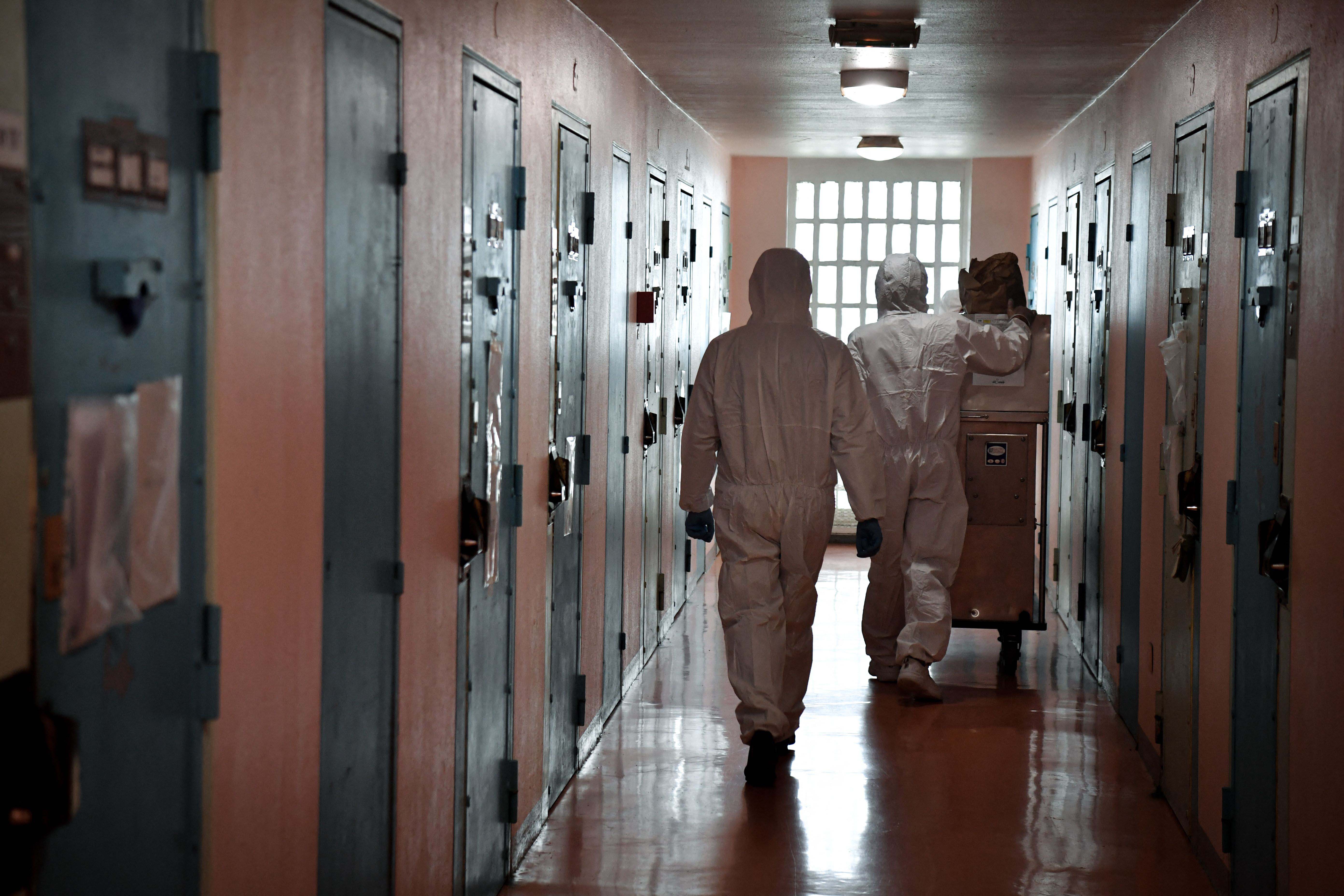 Two people in PPE walk down a prison corridor