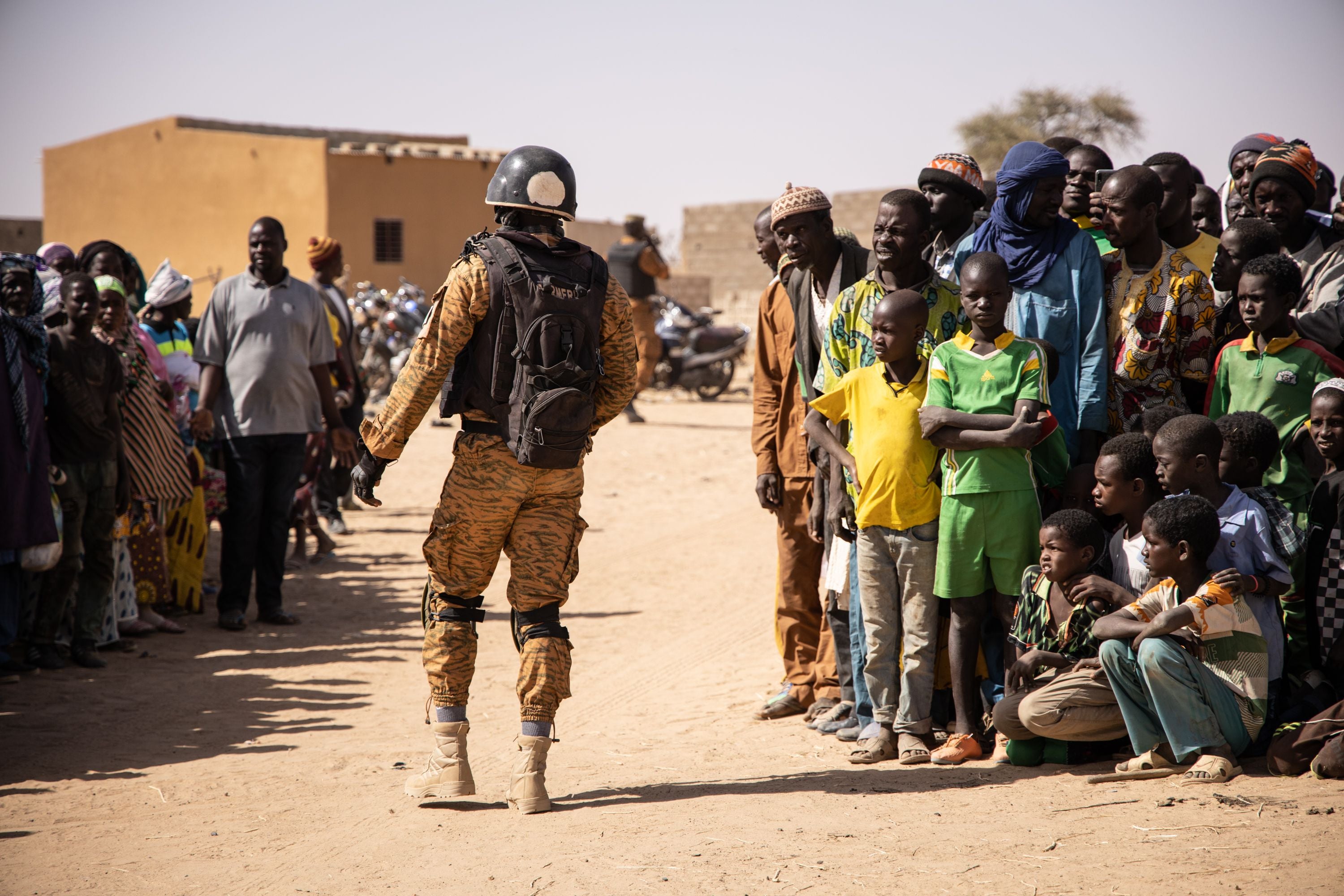 A government soldier walks past a group of villagers displaced by fighting in Burkina Faso’s northern Sahel region, February 3, 2020. 
