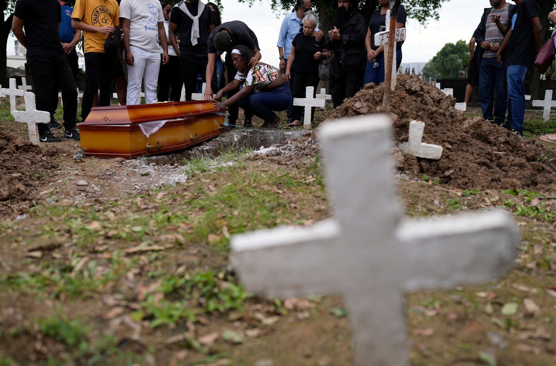 People stand and kneel next to a casket in a cemetery