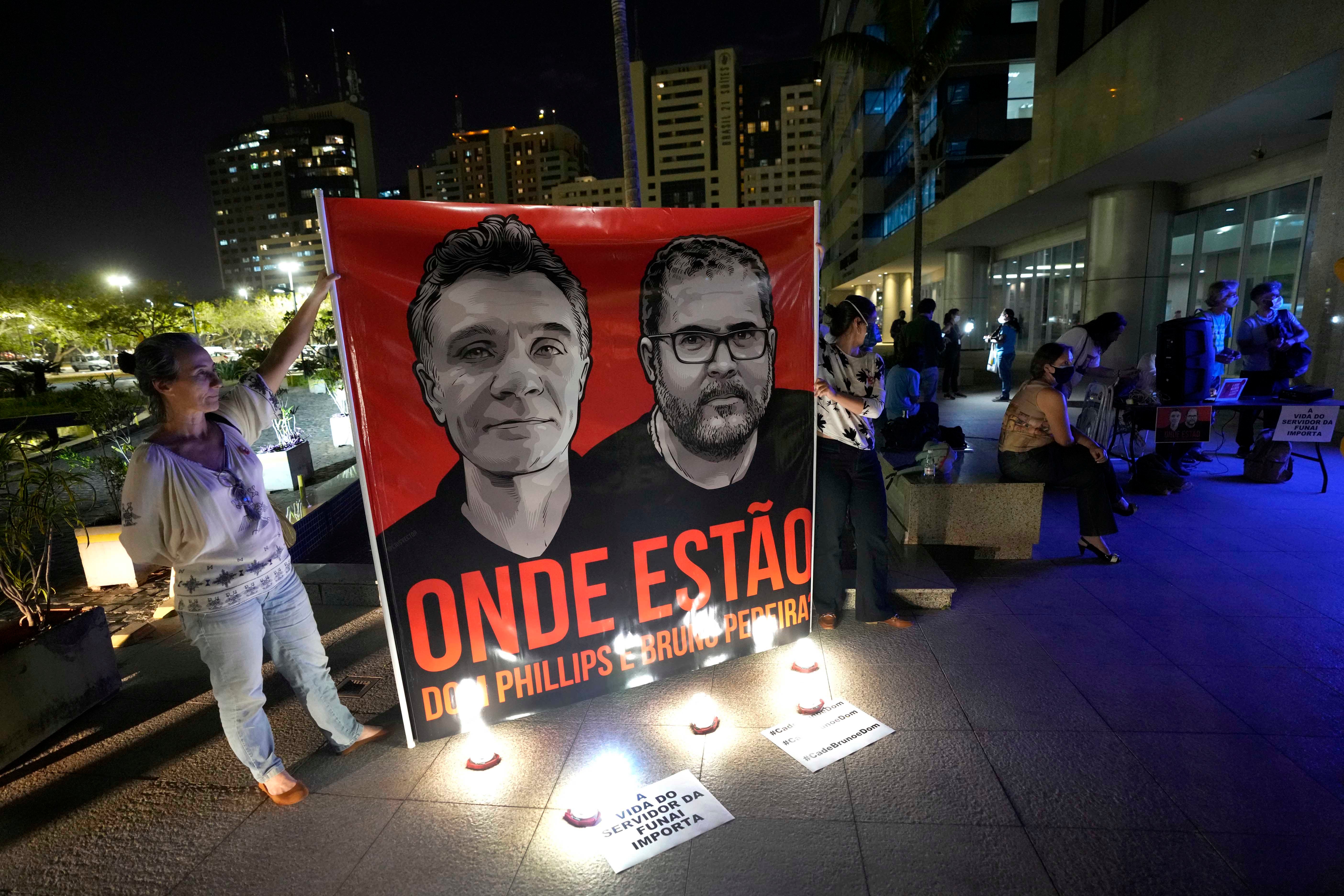 People display a large poster with images of Dom Phillips and Bruno Pereira