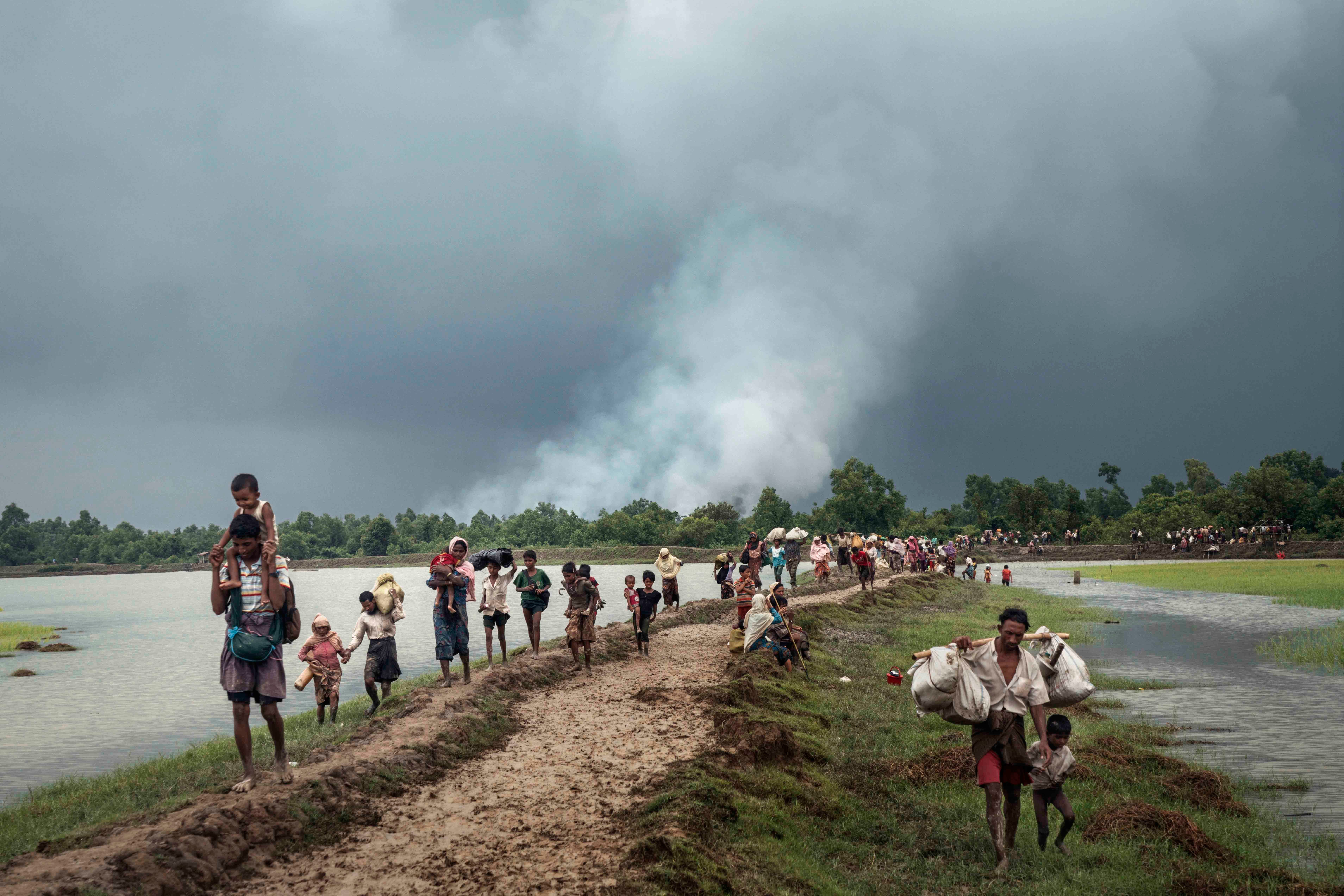 Refugees walk next to a river