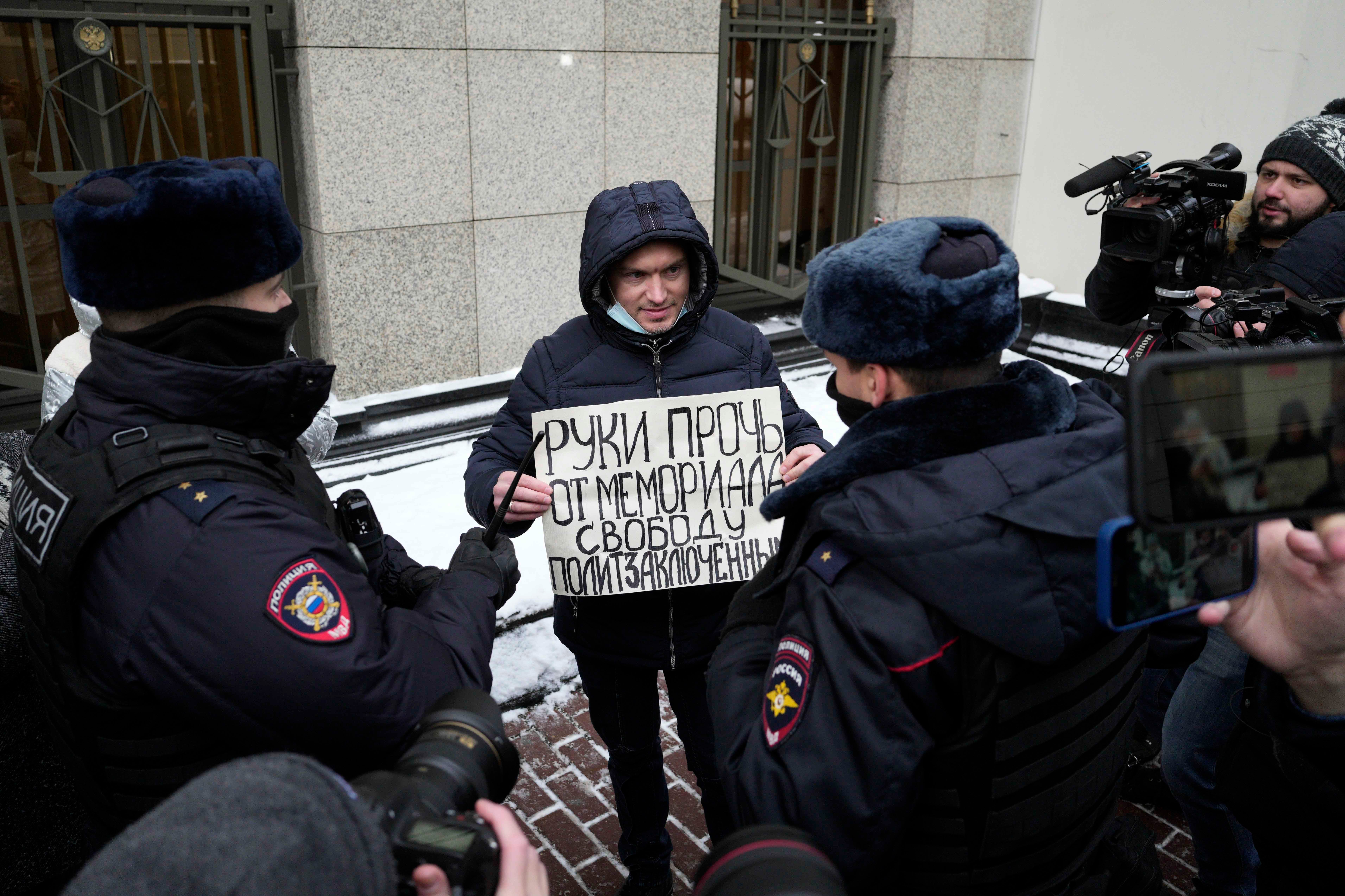 Police officers detain a demonstrator holding a poster reading "Hands off Memorial, freedom for political prisoners"