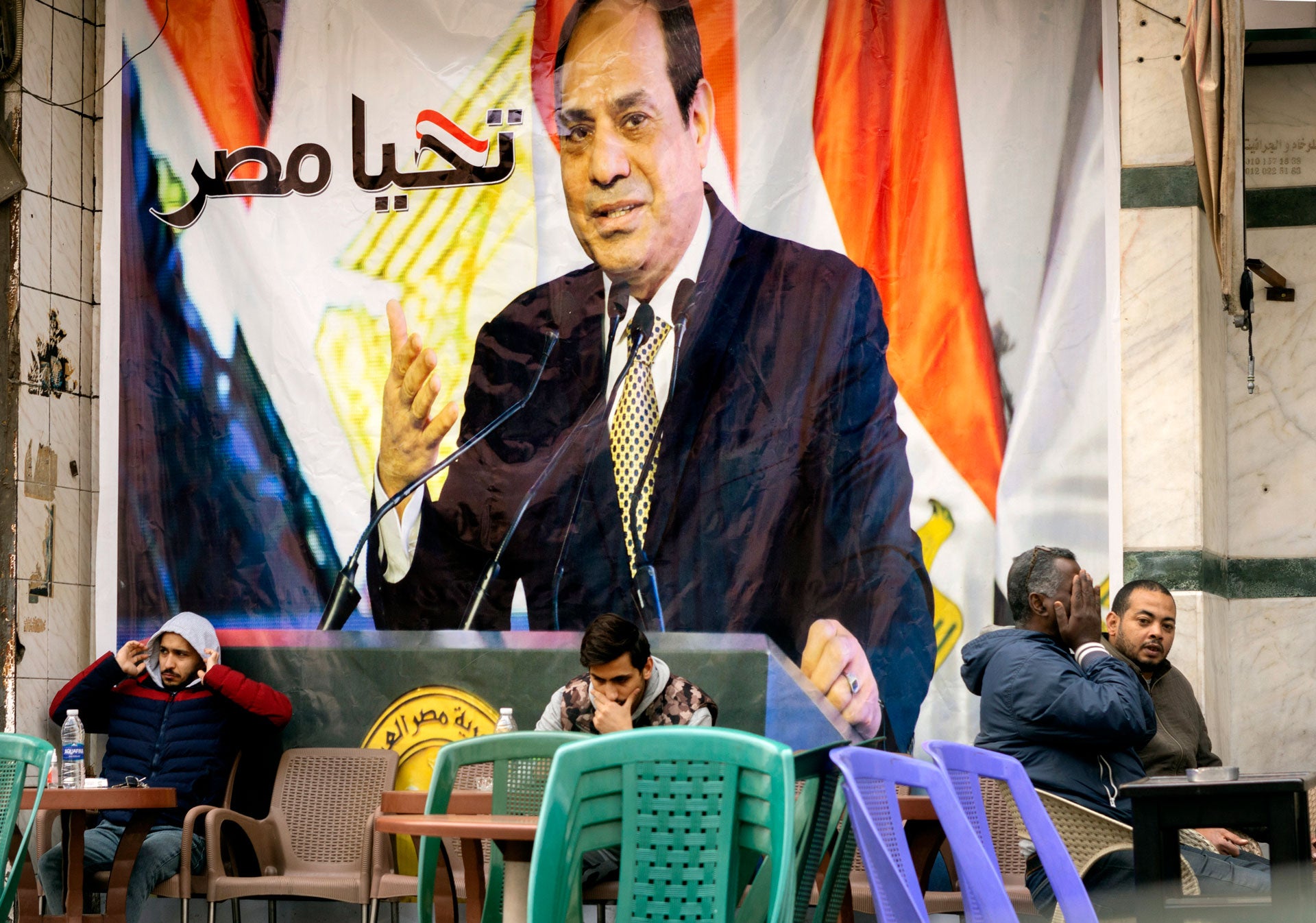 People sit under a banner with a picture of Egyptian President Abdel Fattah al-Sisi that reads, "Long live Egypt"