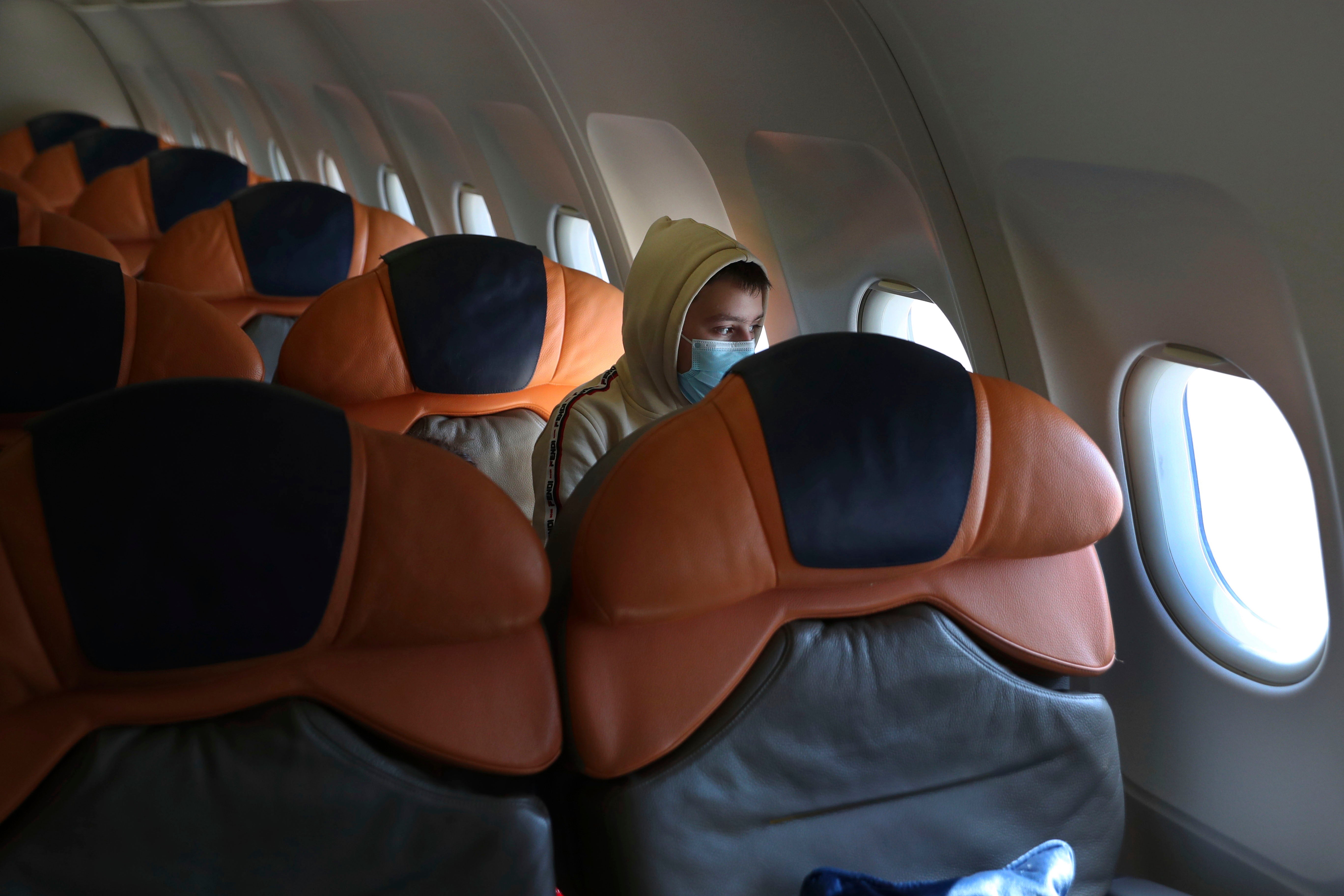 A boy in a face mask sits alone on an airplane