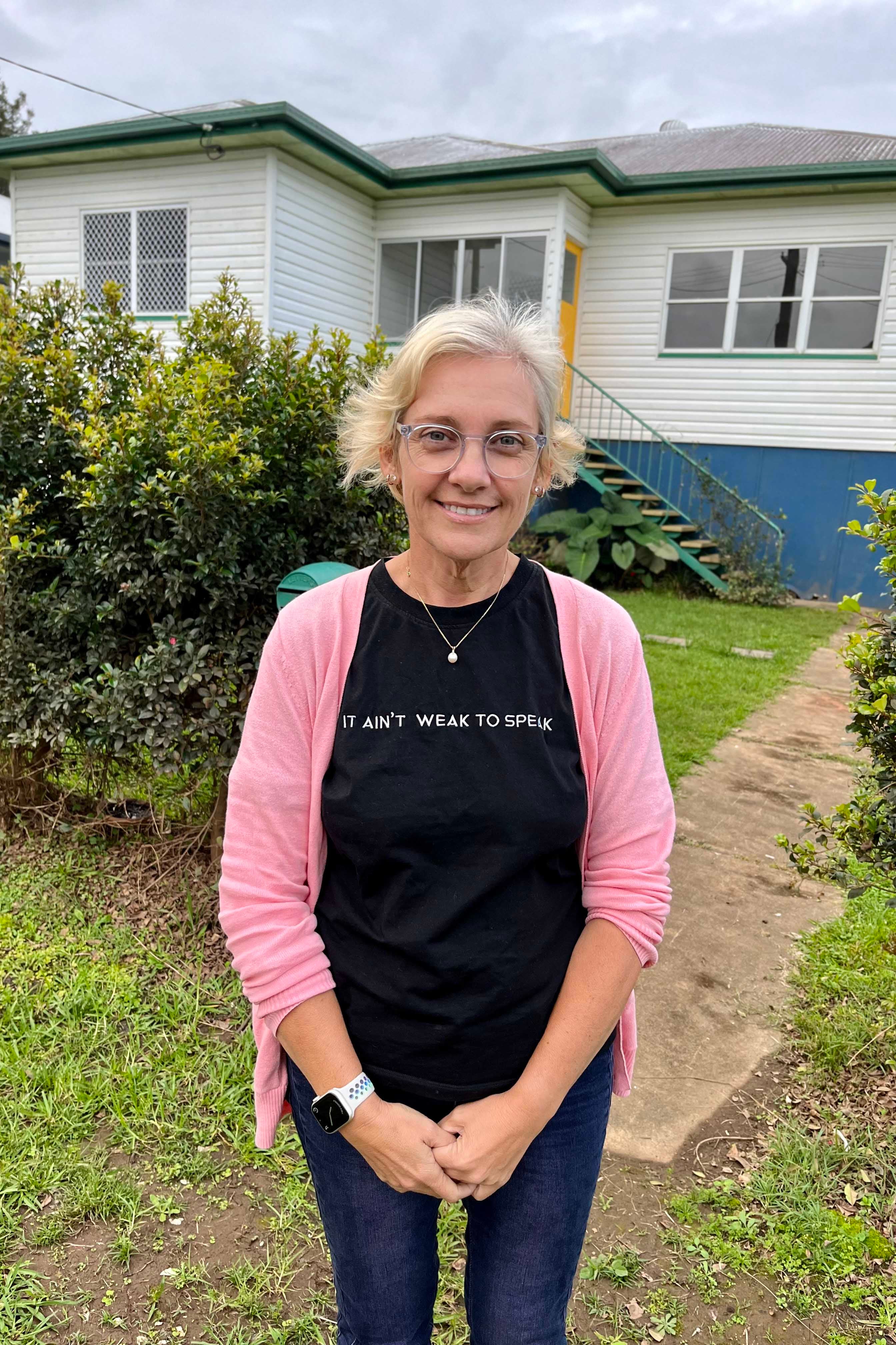 A woman stands in front of her house