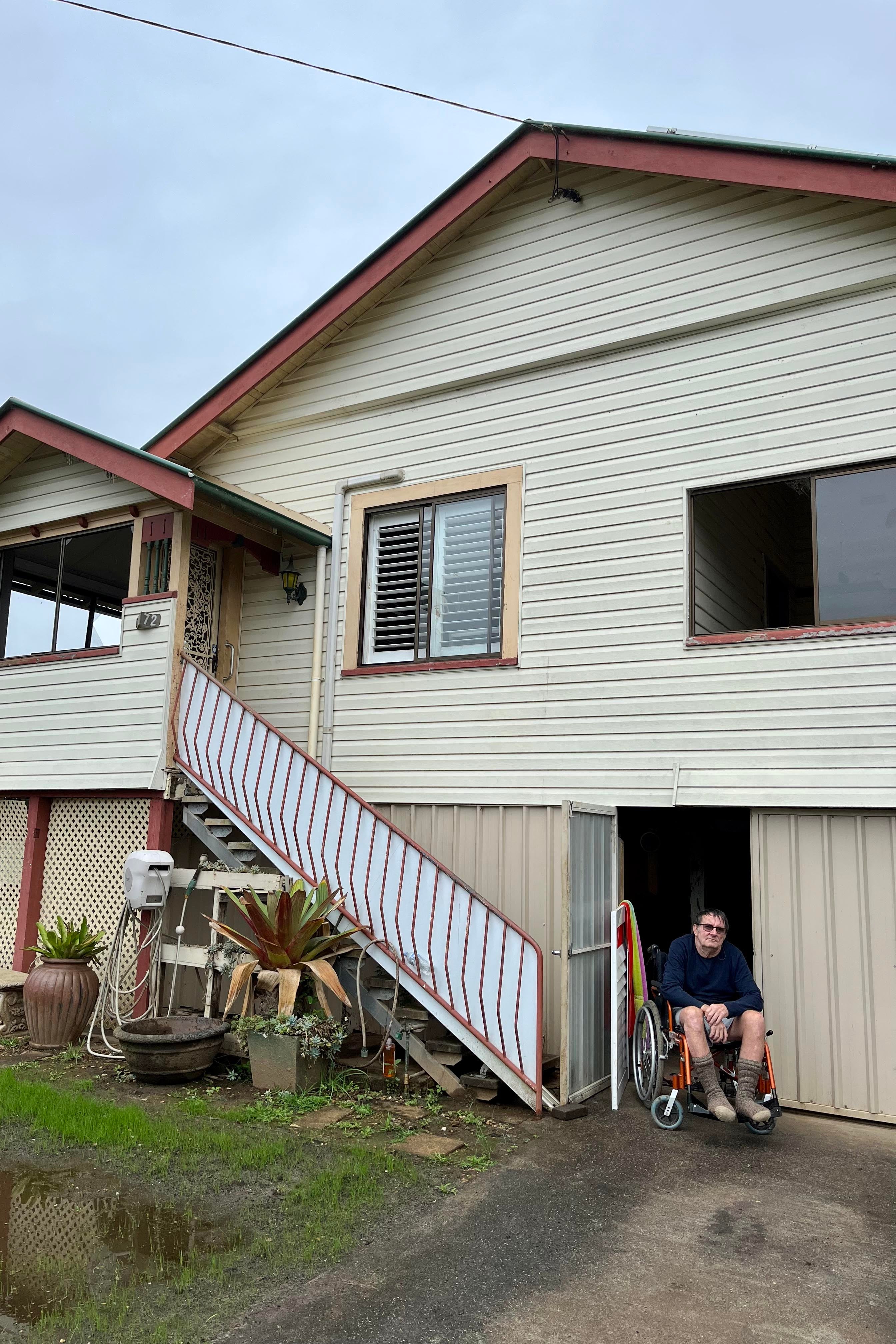 A man sits in his wheelchair in front of his house