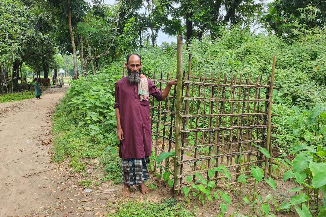 An older man stands beside a grave