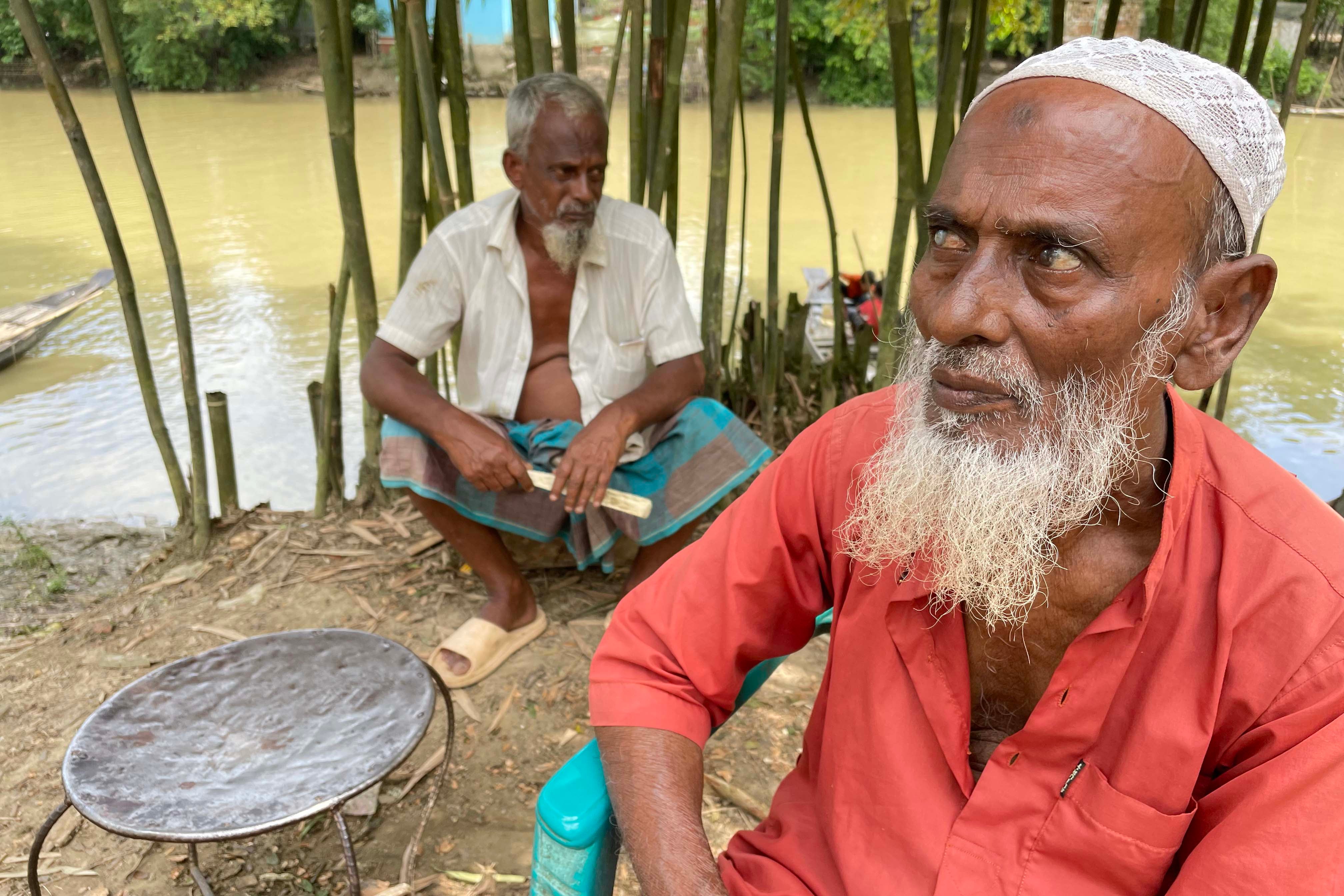 Two older men sit near a river