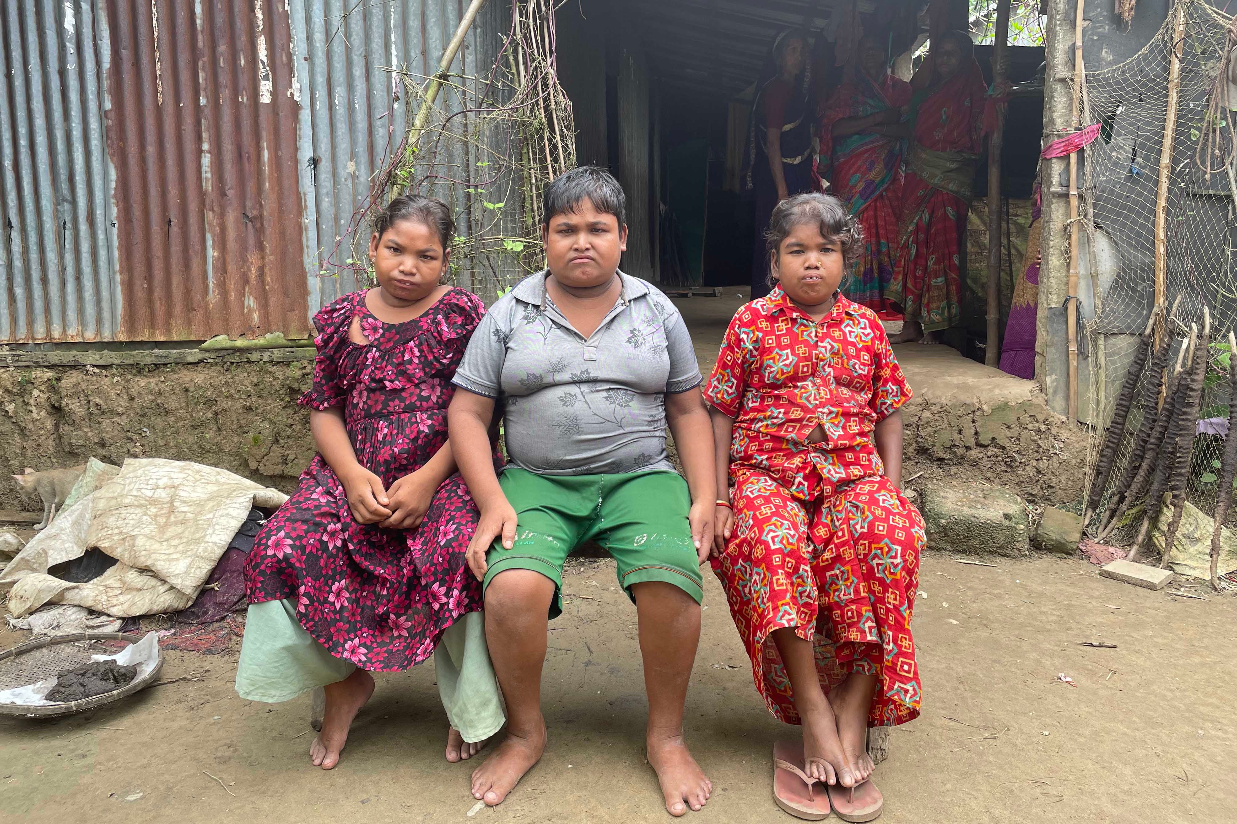 Three young people sit in front of their house