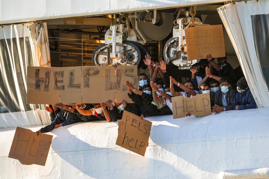 Migranti con in mano cartelli che chiedono aiuto, da un ponte della nave Geo Barents, battente bandiera norvegese e gestita da Medici Senza Frontiere, nel porto di Catania, in Sicilia, Italia meridionale, 7 Novembre 2022.