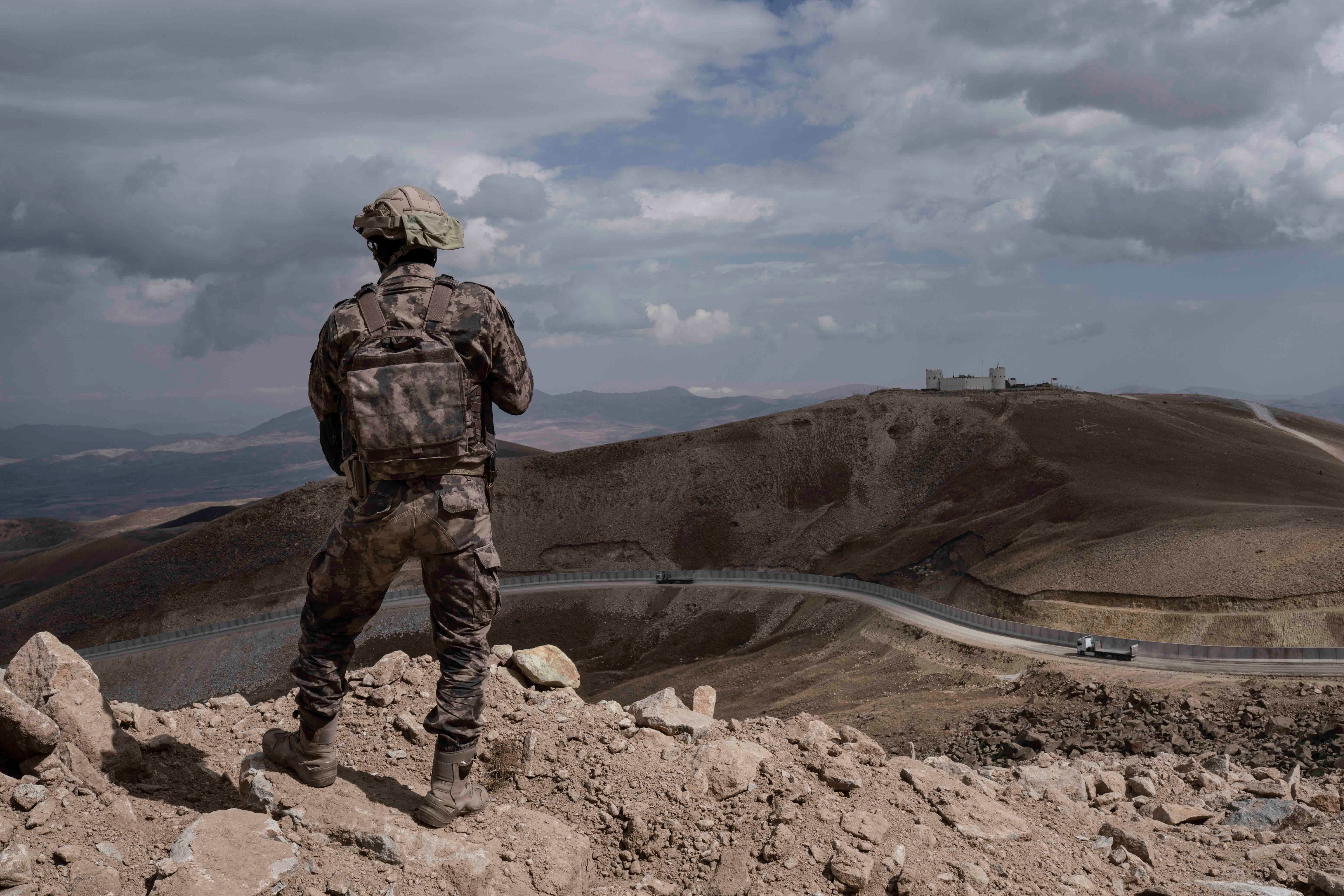 A uniformed soldier stands on a hill above a border wall 
