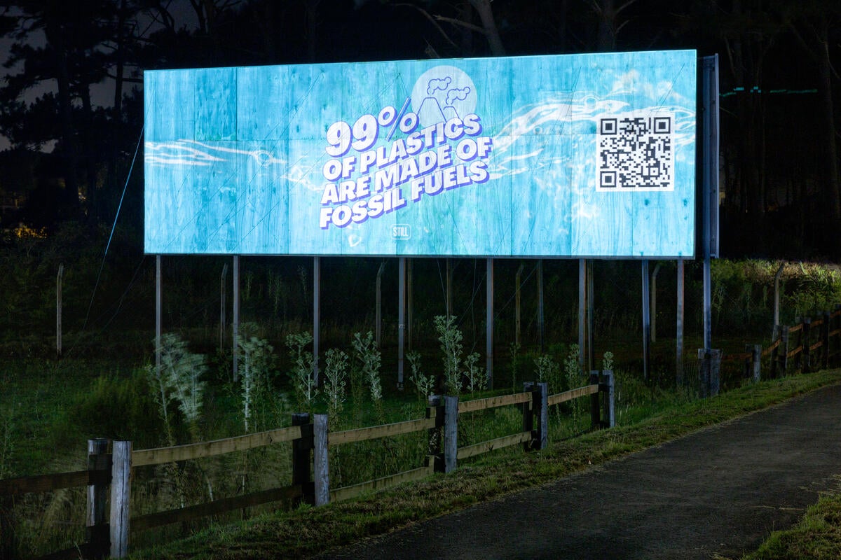 A billboard with the message "99% of plastics are made of fossil fuels" projected on