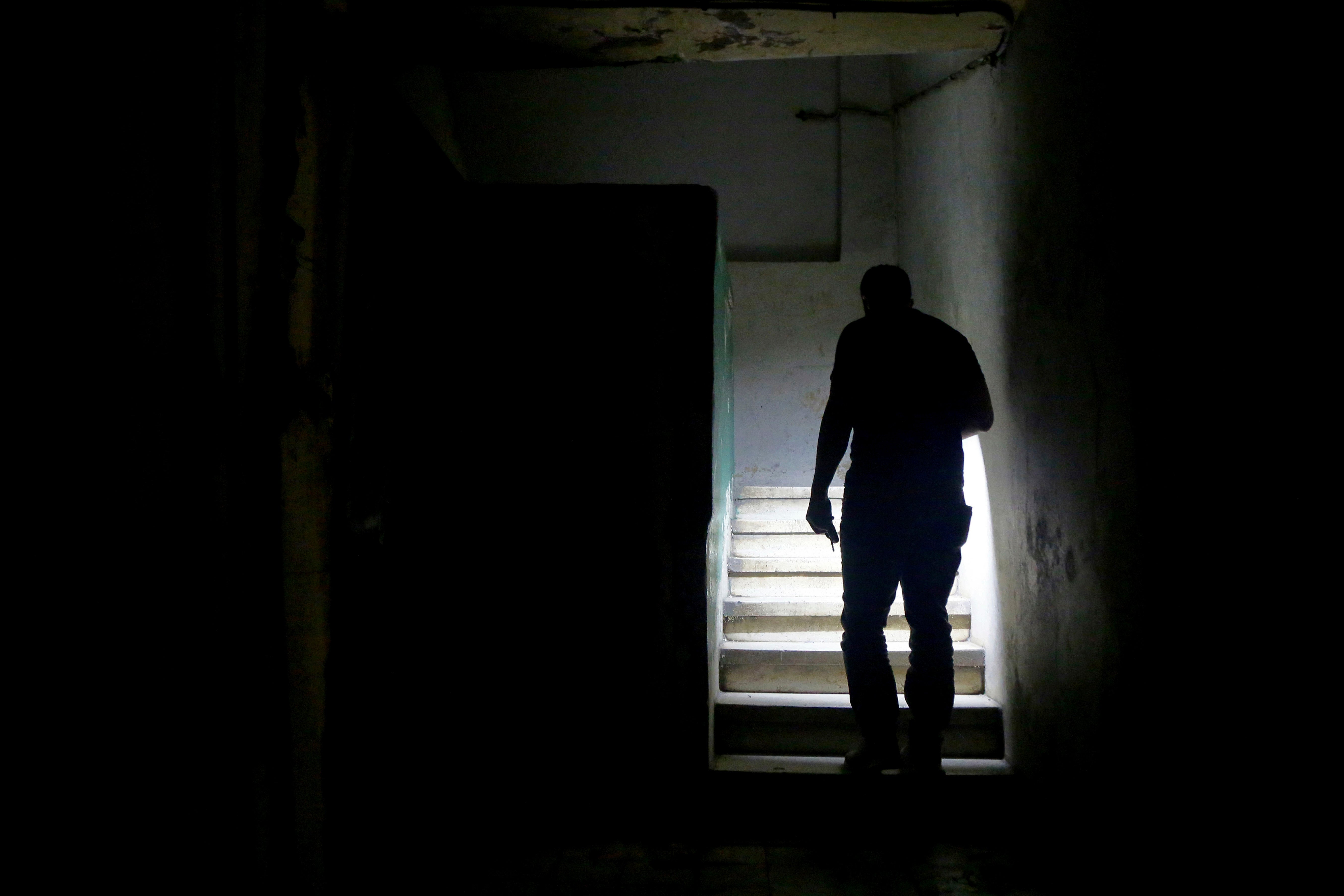 A man uses his mobile phone torch to walk up the stairs to reach his apartment