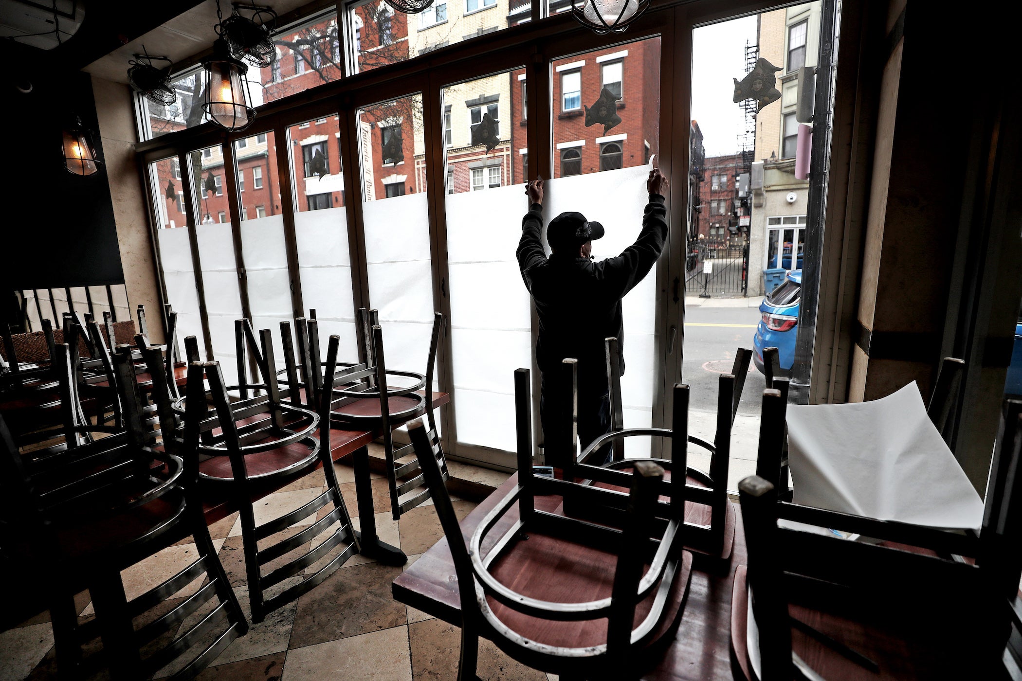 Un empleado de Carmelina's, en el extremo norte de Boston, pega con cinta adhesiva papeles en las ventanas del restaurante que cerró temporalmente durante la pandemia de coronavirus. 25 de marzo de 2020.