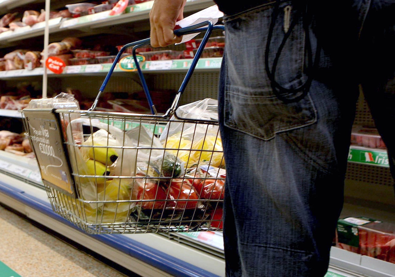 A person holding a shopping basket in a supermarket.