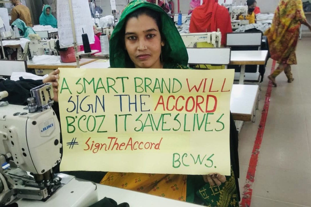 A garment factory worker in Bangladesh holds a sign to stand up for safe factories and the International Health and Safety Accord