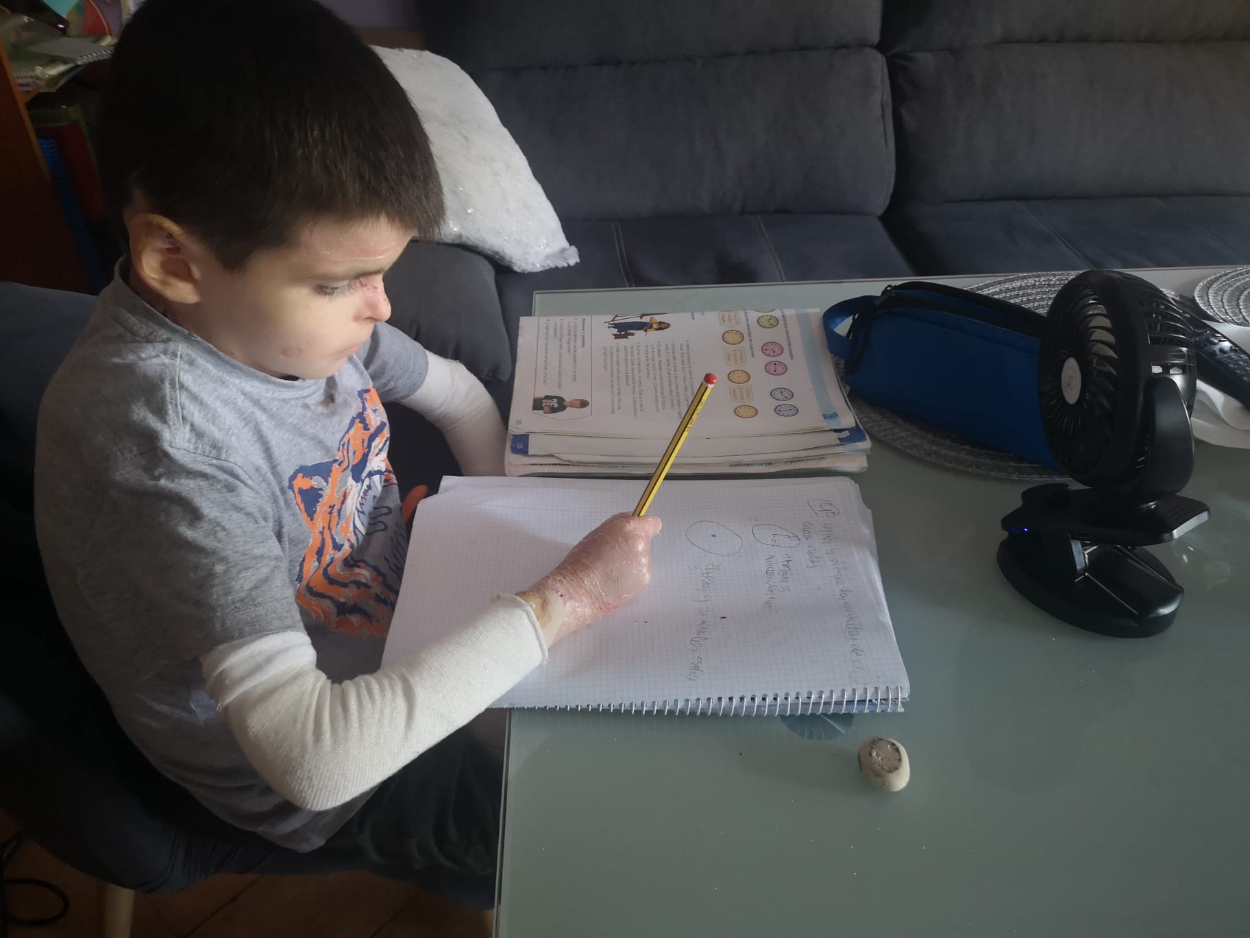 Leo Osorio, de 9 años, quien tiene una discapacidad física, hace la tarea en la sala de su vivienda en Sevilla (Andalucía, España), con un ventilador pequeño para mantenerse fresco.