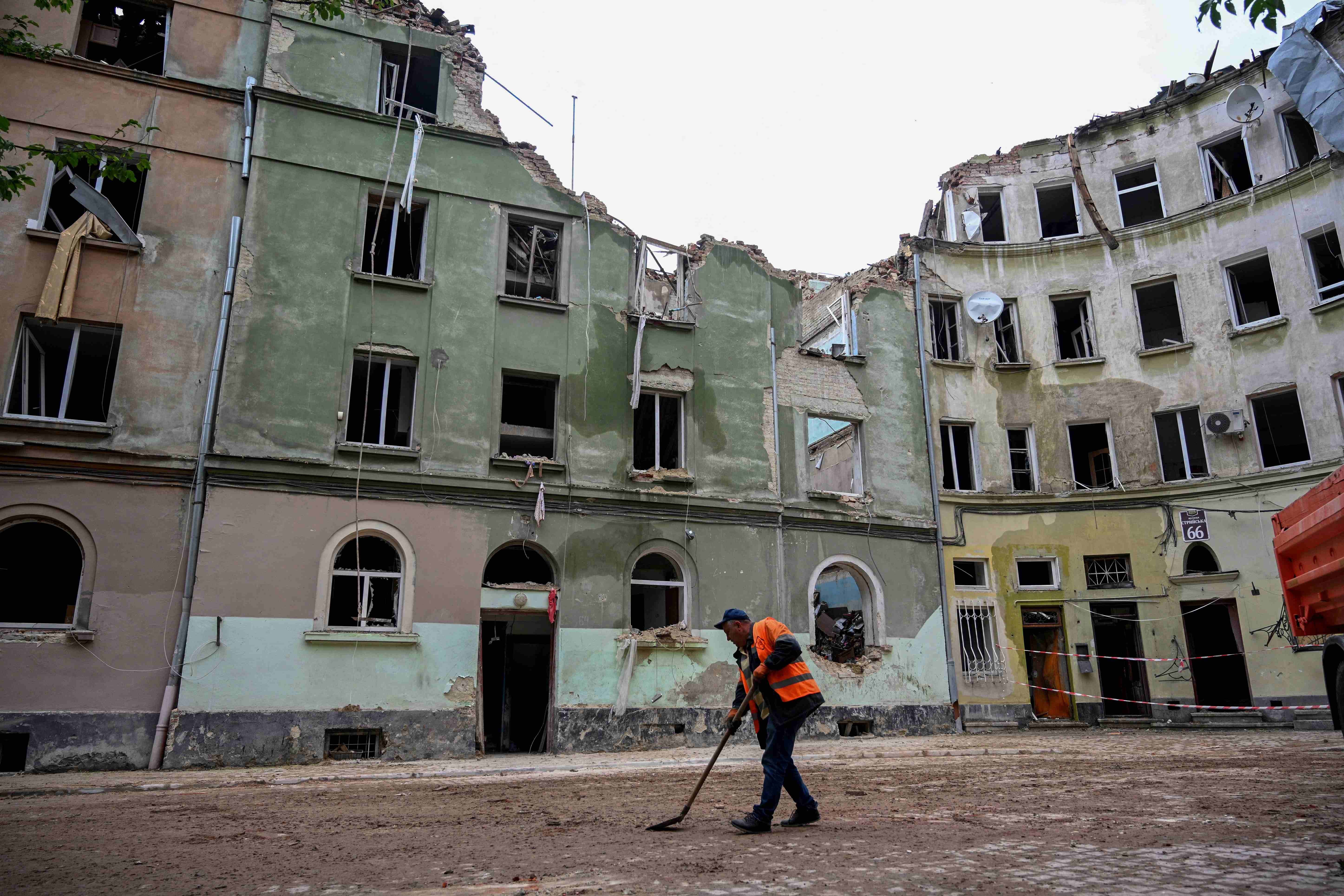 Львов, 7 июля 2023 г. Сотрудник коммунальных служб подметает двор дома, получившего накануне серьезные повреждения в результате российского ракетного удара. 
