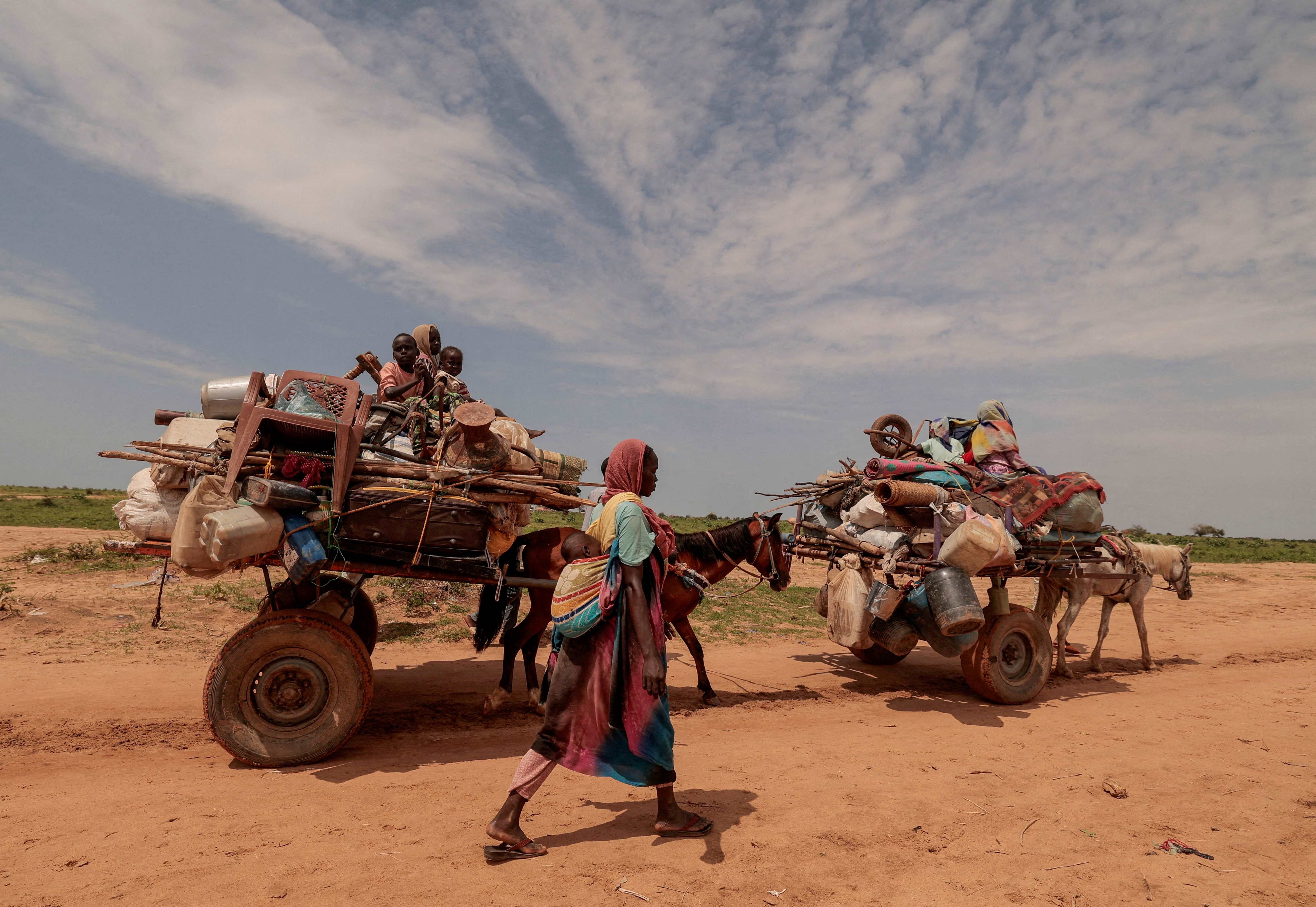 امرأة سودانية كانت قد غادرت مورني في منطقة دارفور هربا من النزاع تمشي بجانب عربات تحمل أمتعة عائلتها أثناء عبور الحدود بين السودان وتشاد في أدري، تشاد، 2 أغسطس/آب 2023. 