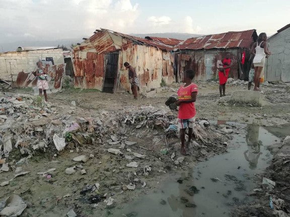 People stand in a muddy street littered with garbage