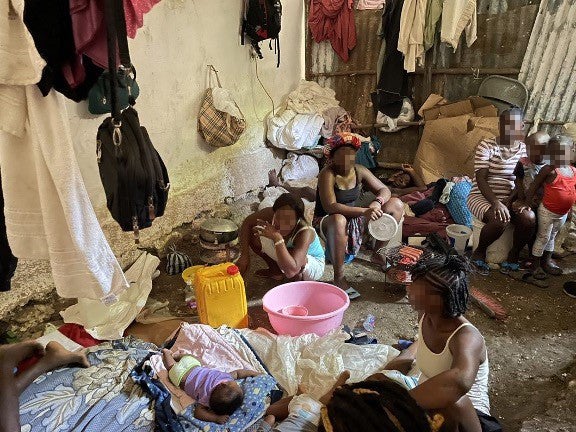 A group of women and children sit in a makeshift shelter