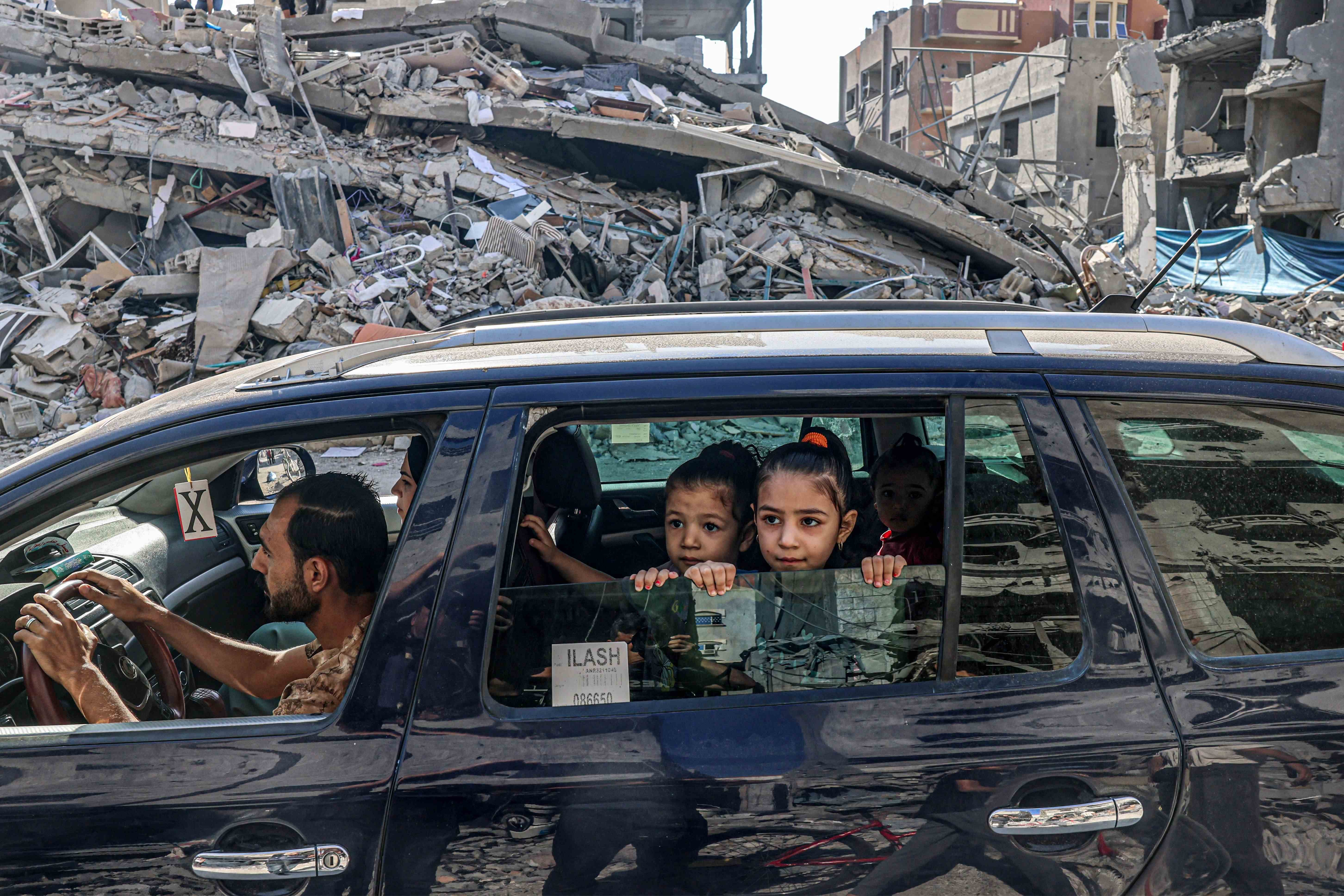 A family in a car drives passed destroyed buildings