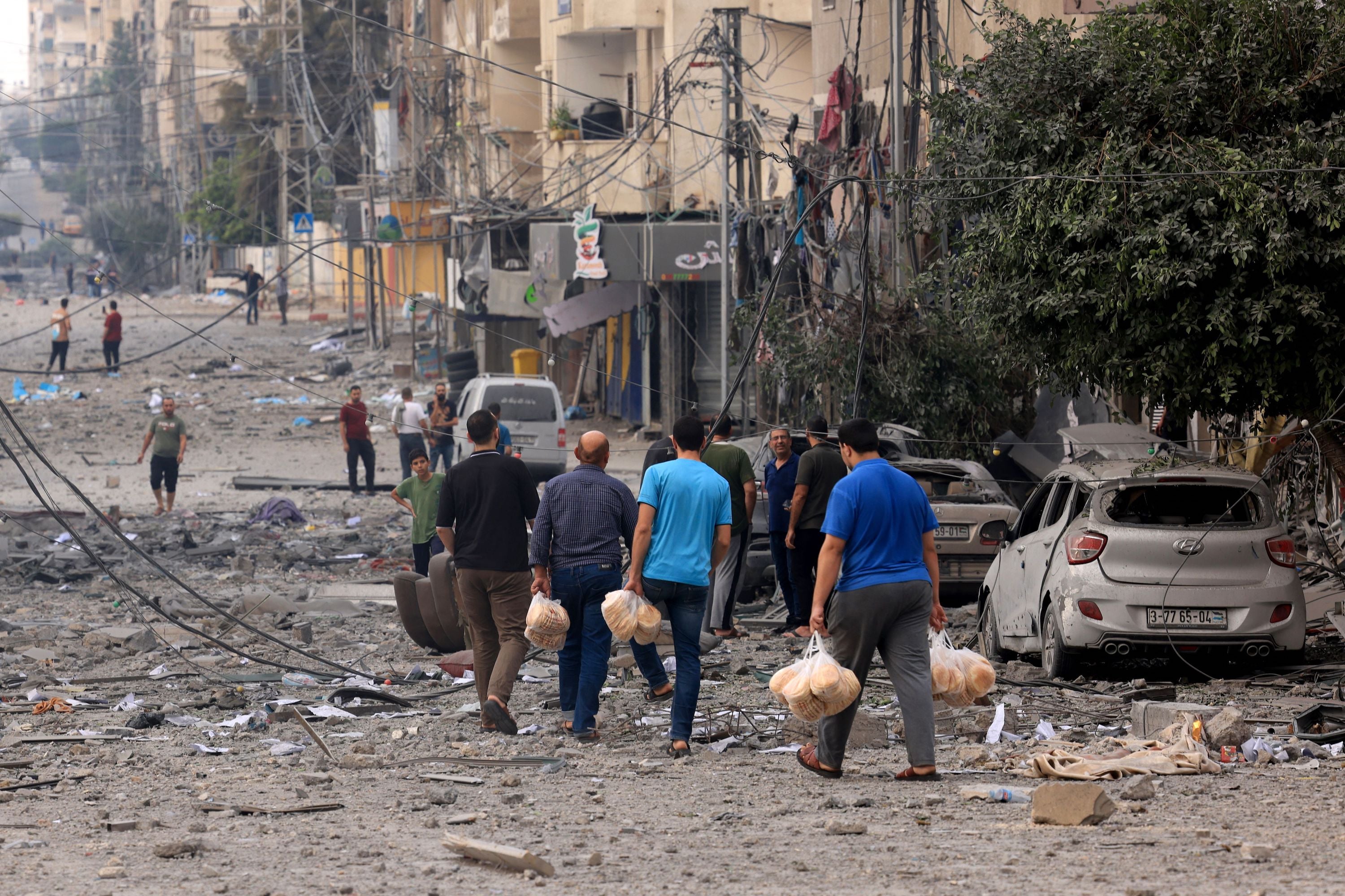  Palestinian men carry bread through a heavily bombed street following Israeli airstrikes on Gaza City on October 10, 2023.  