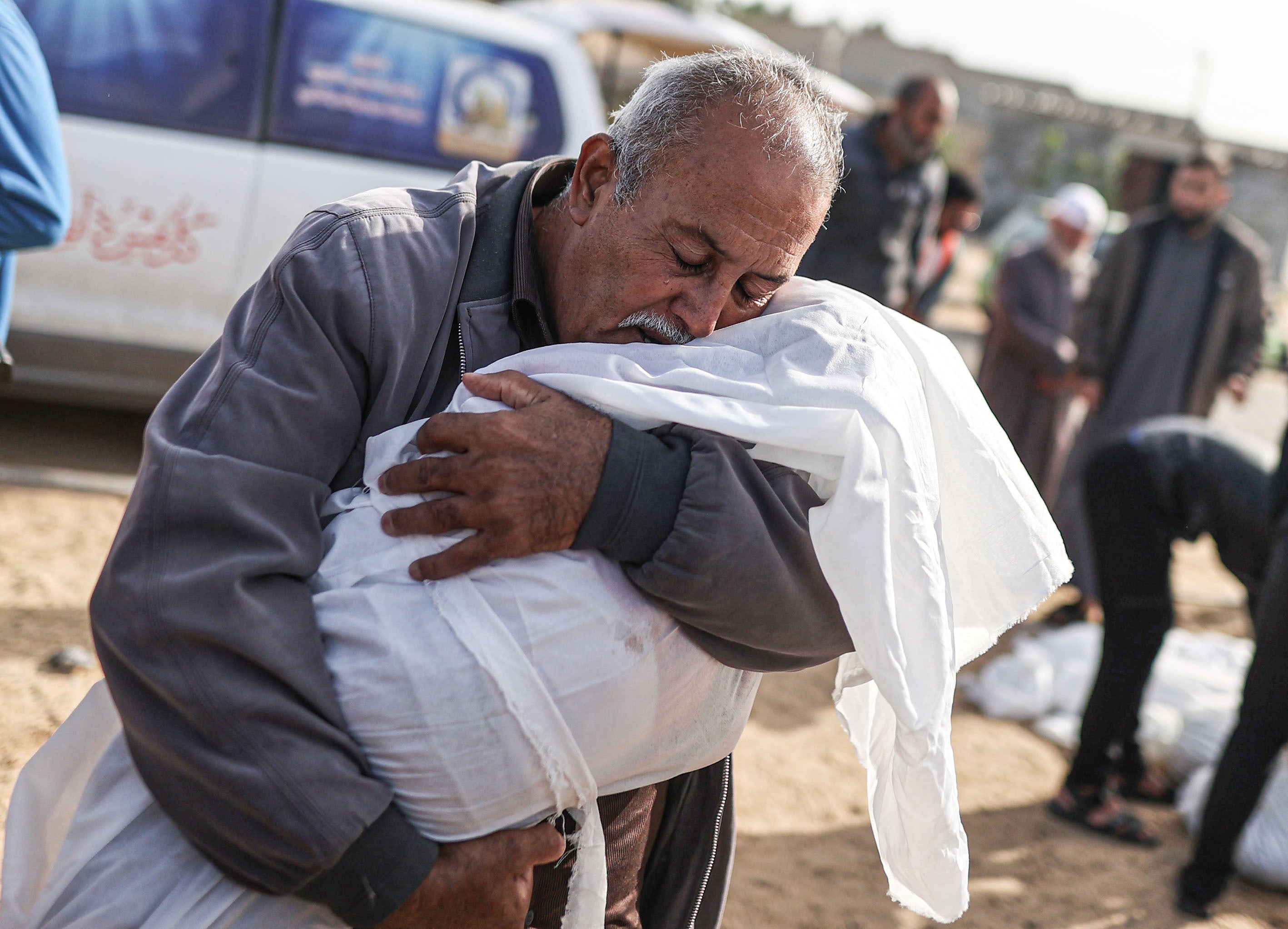 Ein Mann umarmt den leblosen Körper eines Kindes, während Palästinenser*innen, die bei israelischen Angriffen getötet wurden, am 22. November 2023 aus der Leichenhalle des Al-Aqsa-Märtyrer-Krankenhauses in Deir al Balah, Gaza, zur Beisetzung herausgebracht werden. 