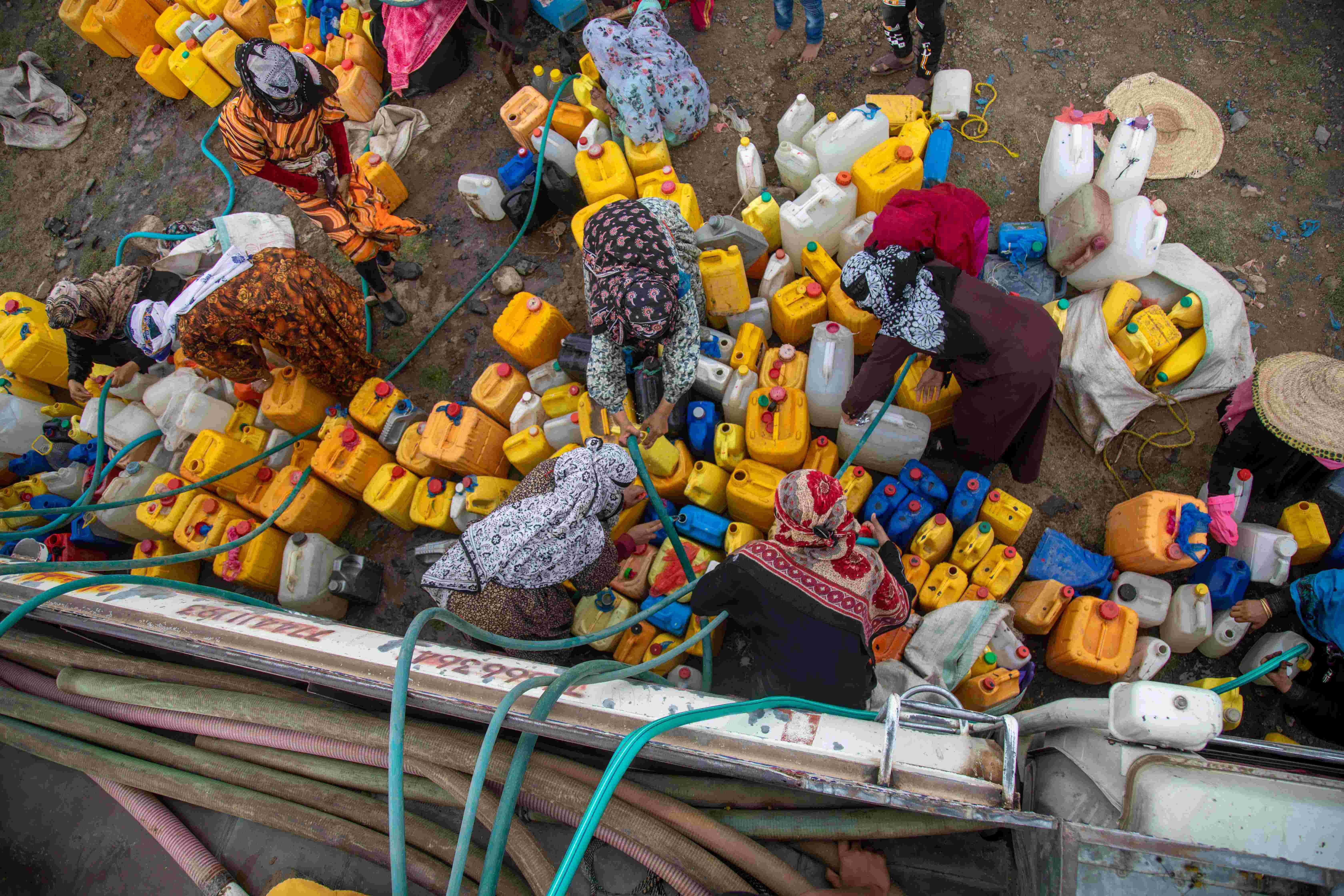 A group of women and children get water from a water truck