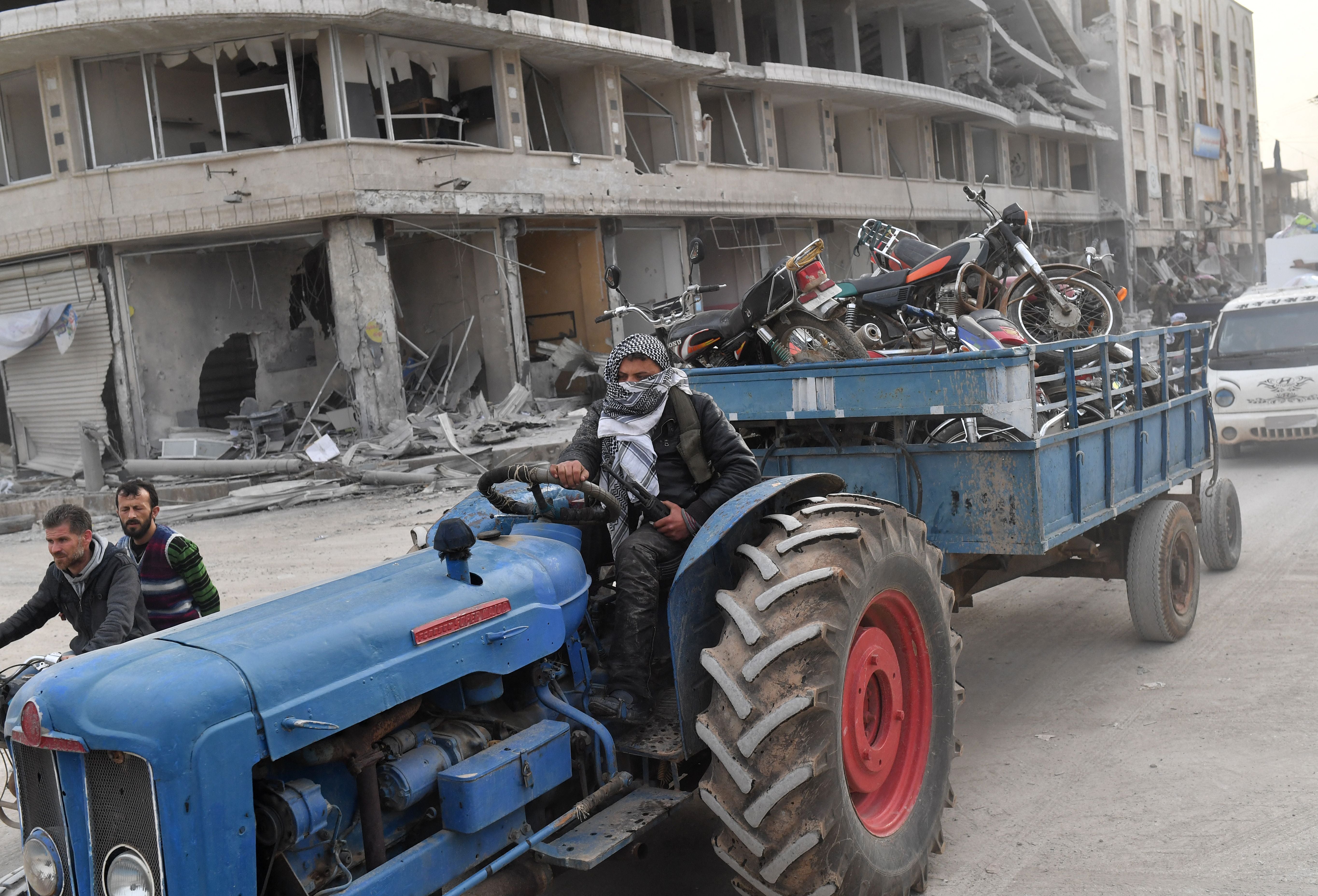 A man wearing a face covering drives a tractor towigng looted items on a trailer