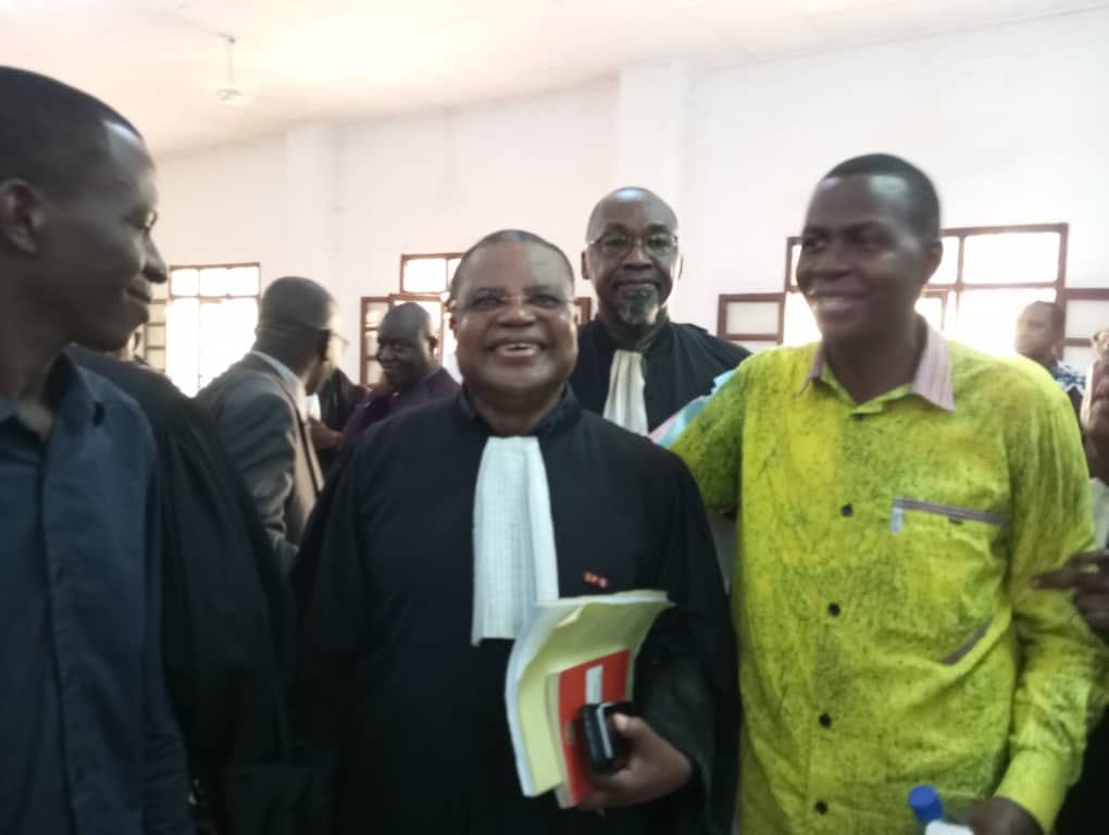 3 men stand smiling in a court room 