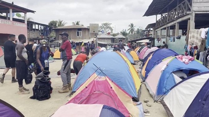 Migrants stand next to tents set up in a rural village