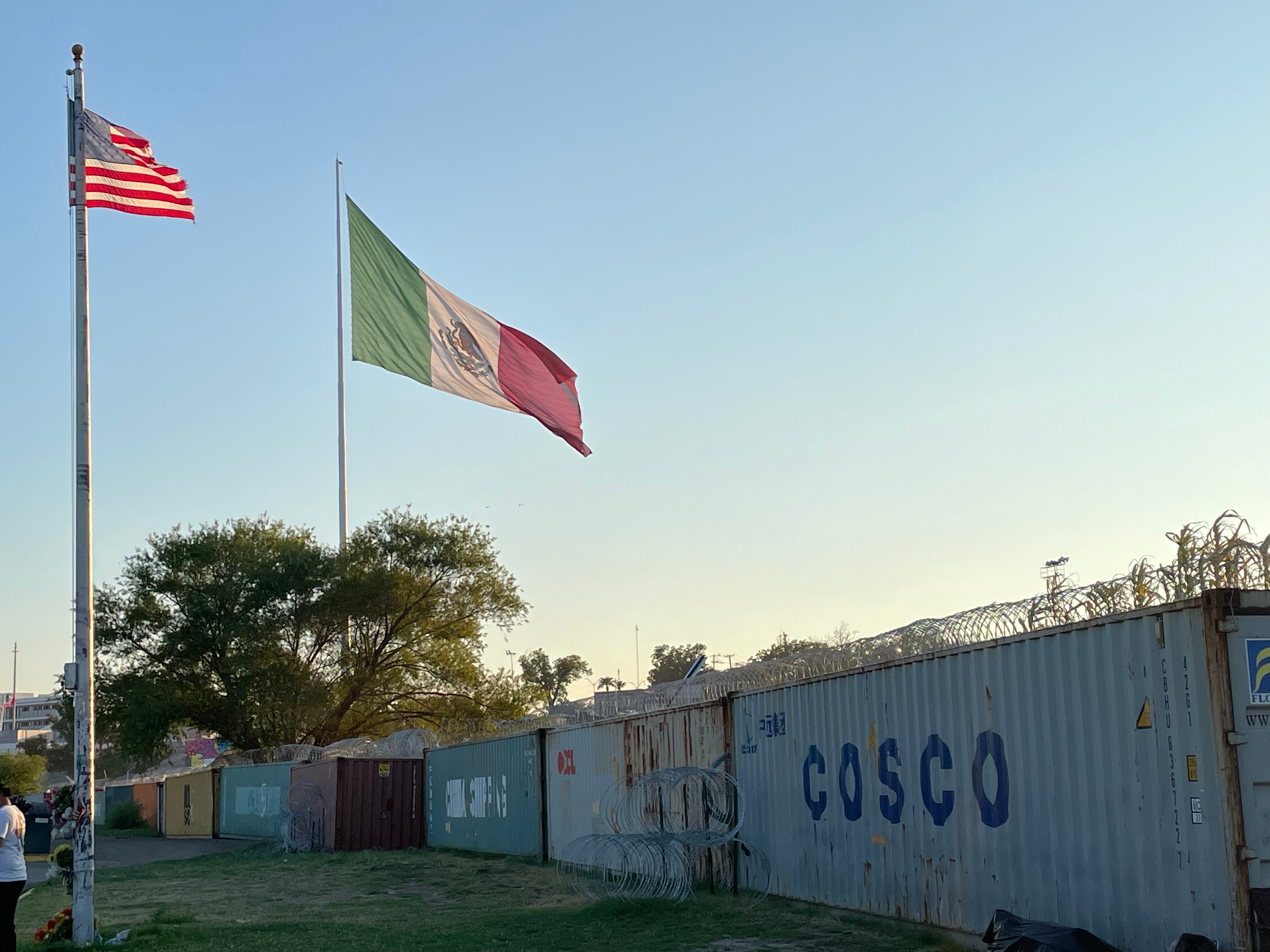 US and Meixco flags flying over a ine of shipping contaniers