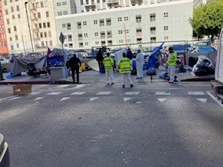 LASAN workers dismantling the encampment as LAPD officers look on.