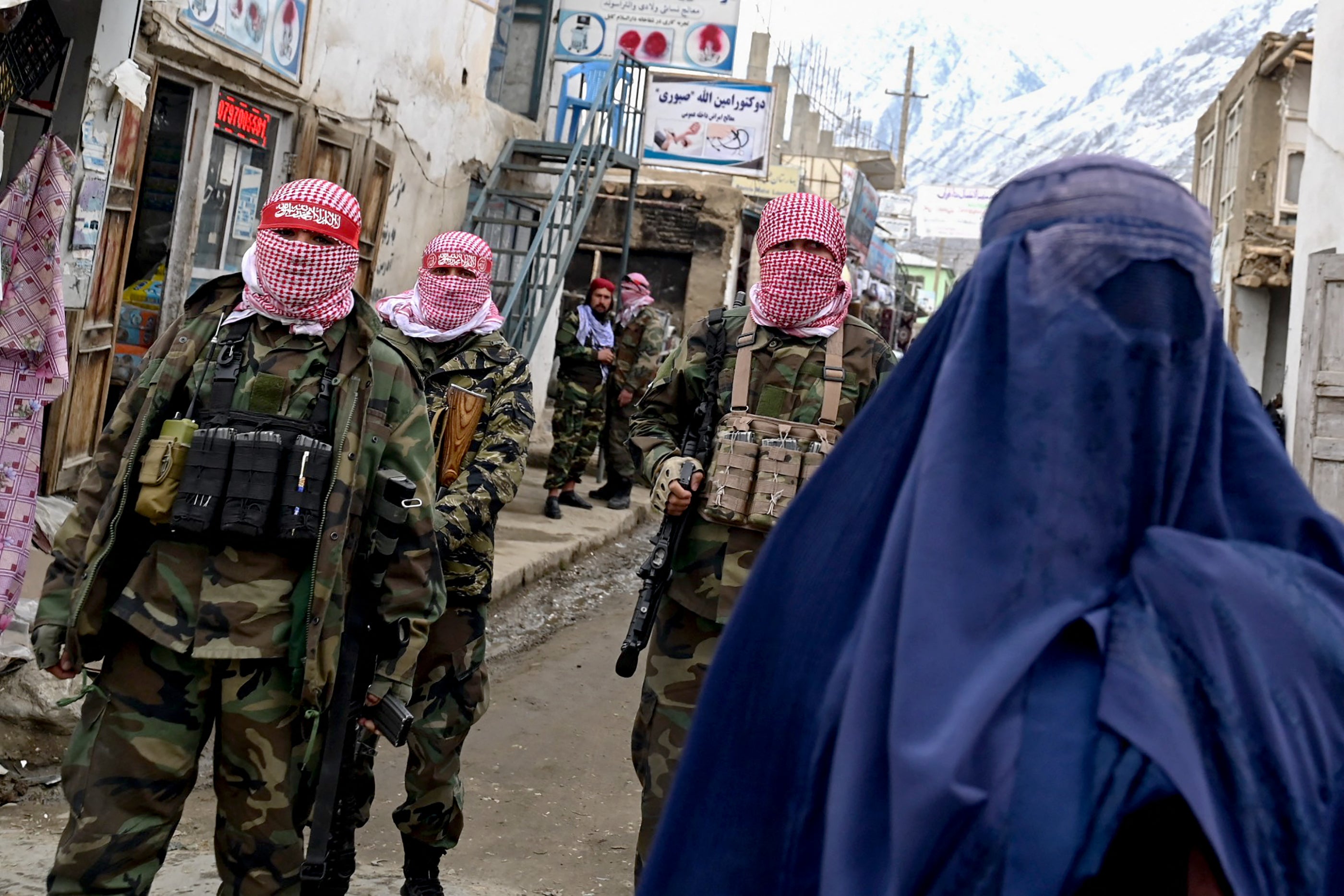 An Afghan woman walks by Taliban security personnel inalong a market in the Baharak district of Badakhshan province, February 26, 2024.