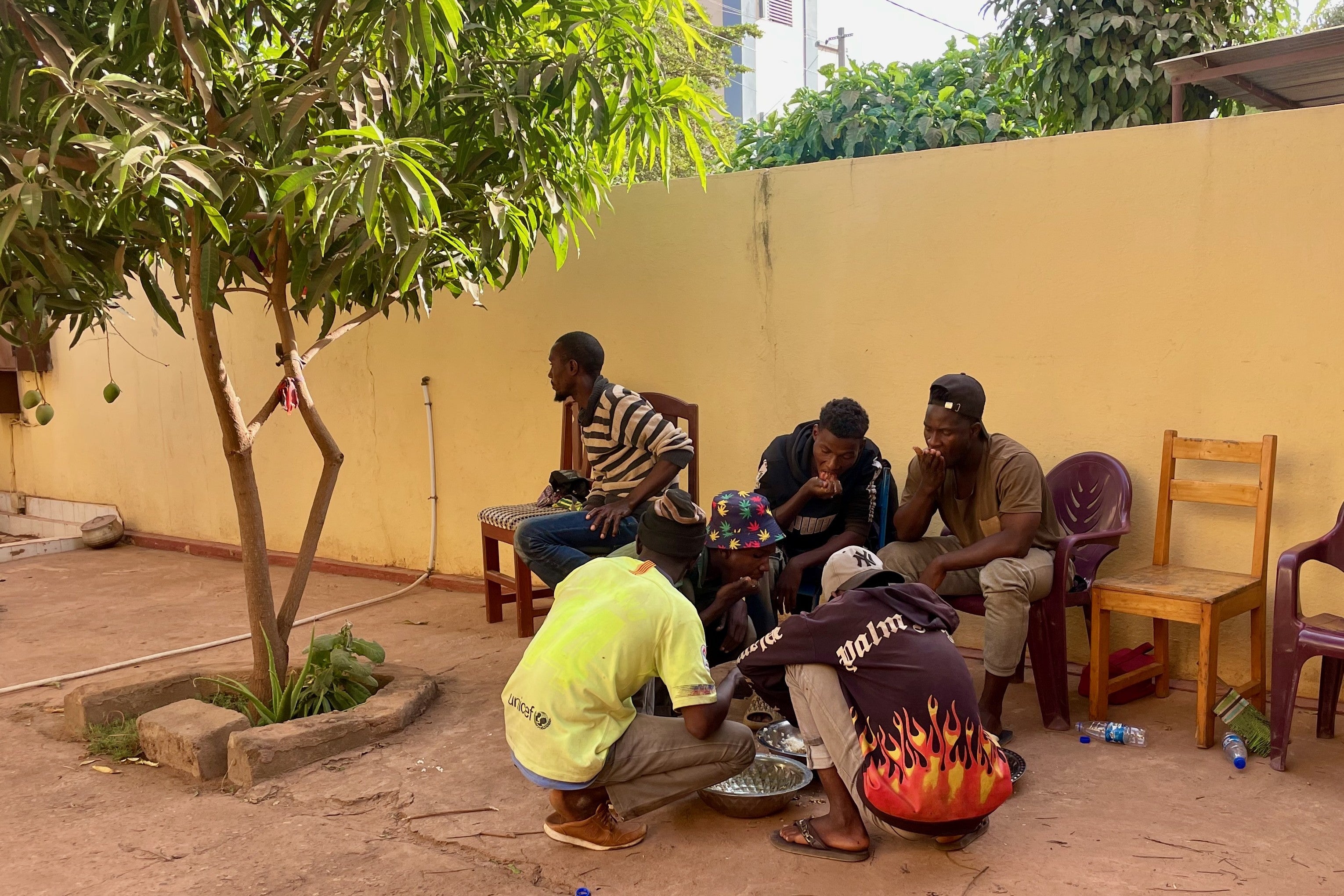 A group of young Guinean men and a 17-year-old boy eat a meal at a shelter 