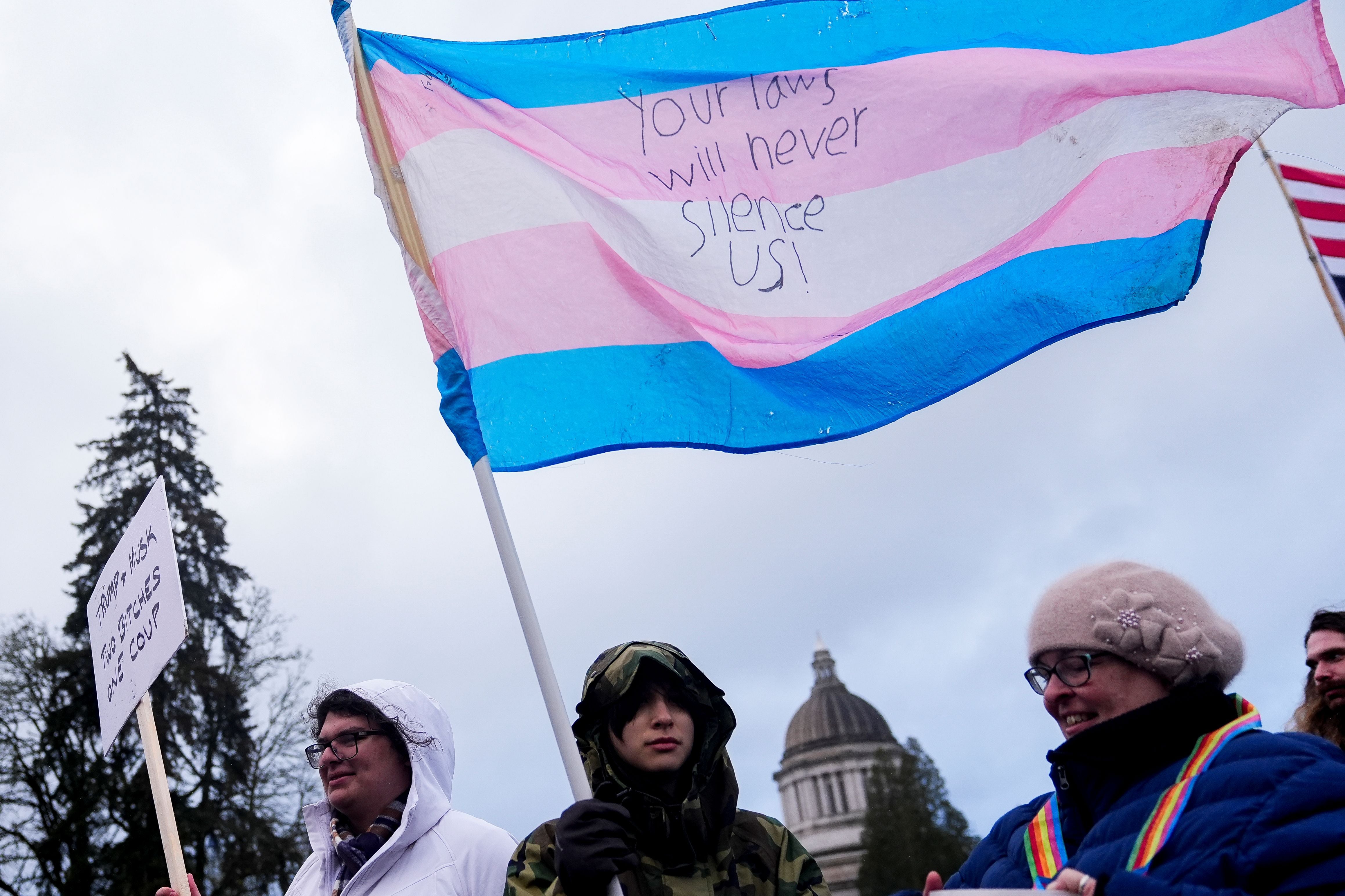 Liv Y., center, holds a transgender pride flag as people gather to protest against the Trump administration near the Washington State Capitol building, in Olympia, Washington, February 5, 2025.