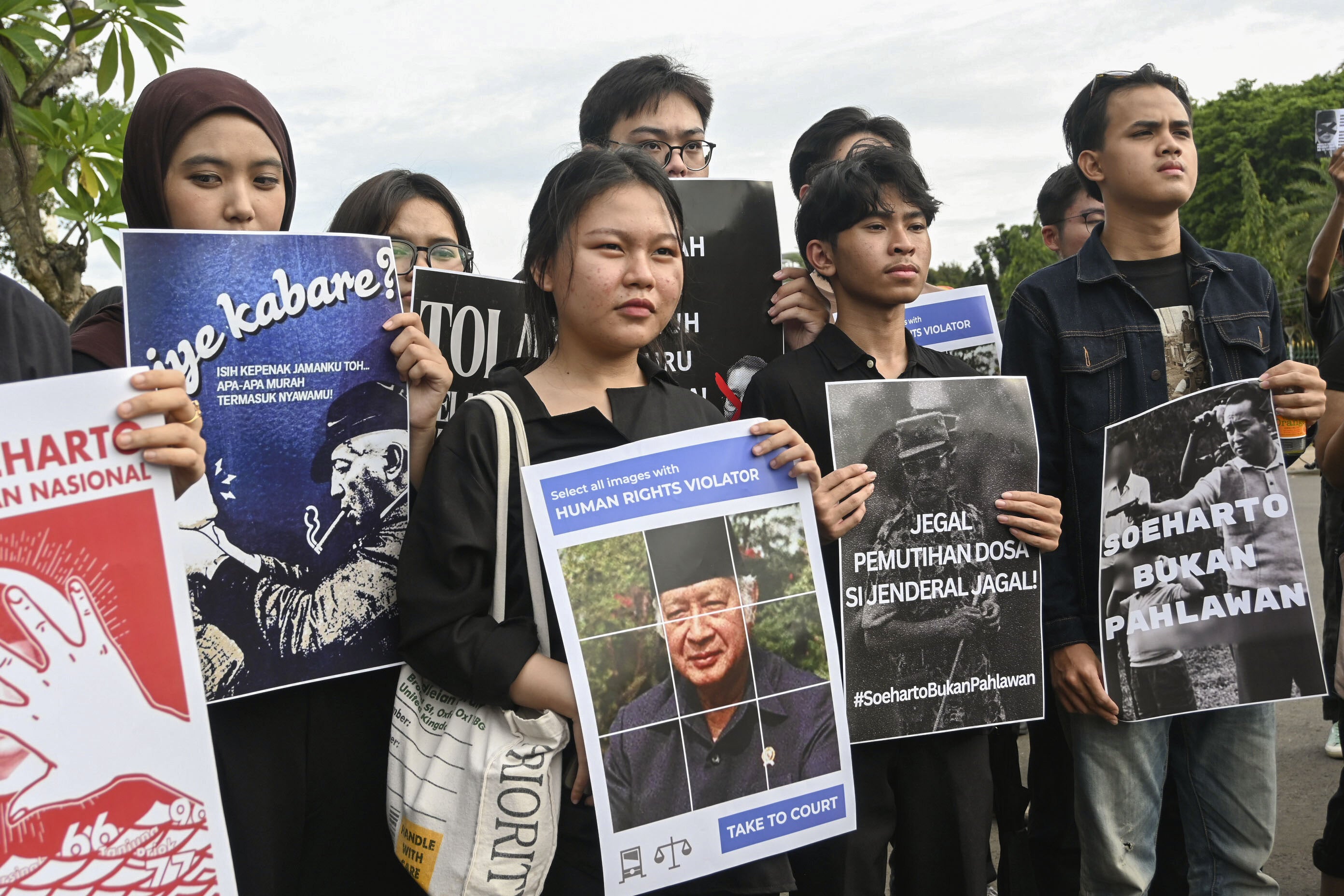 Demonstrators hold placards depicting the late Indonesian President Suharto during a rally against a government proposal to name him a “national hero”