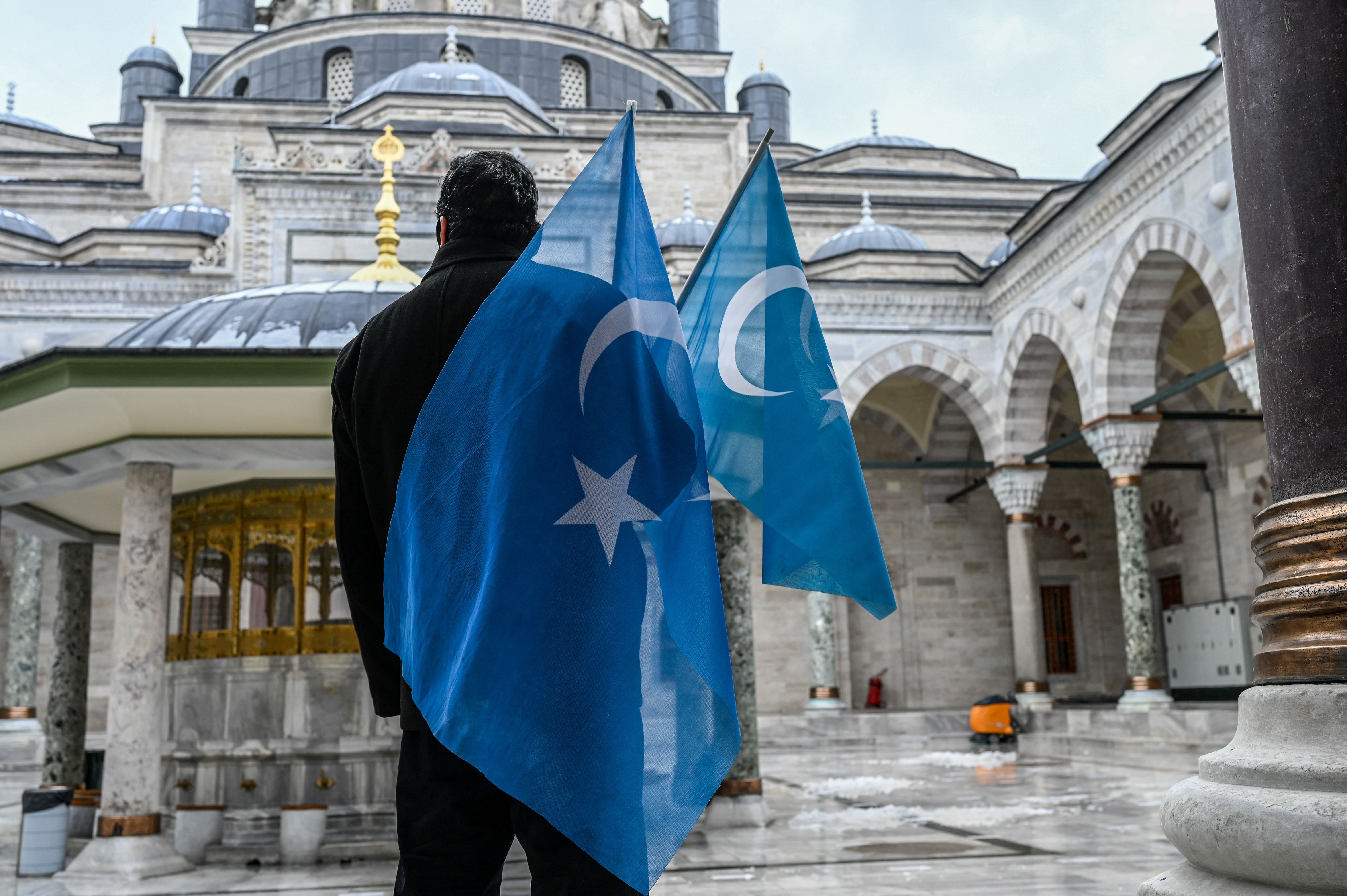 Un membre de la communauté ouïghoure résidant en Turquie tenait deux drapeaux du Turkestan oriental – nom donné par de nombreux Ouighours à la région du Xinjiang en Chine - devant la mosquée Beyazit à Istanbul, le 25 mars 2021. 
