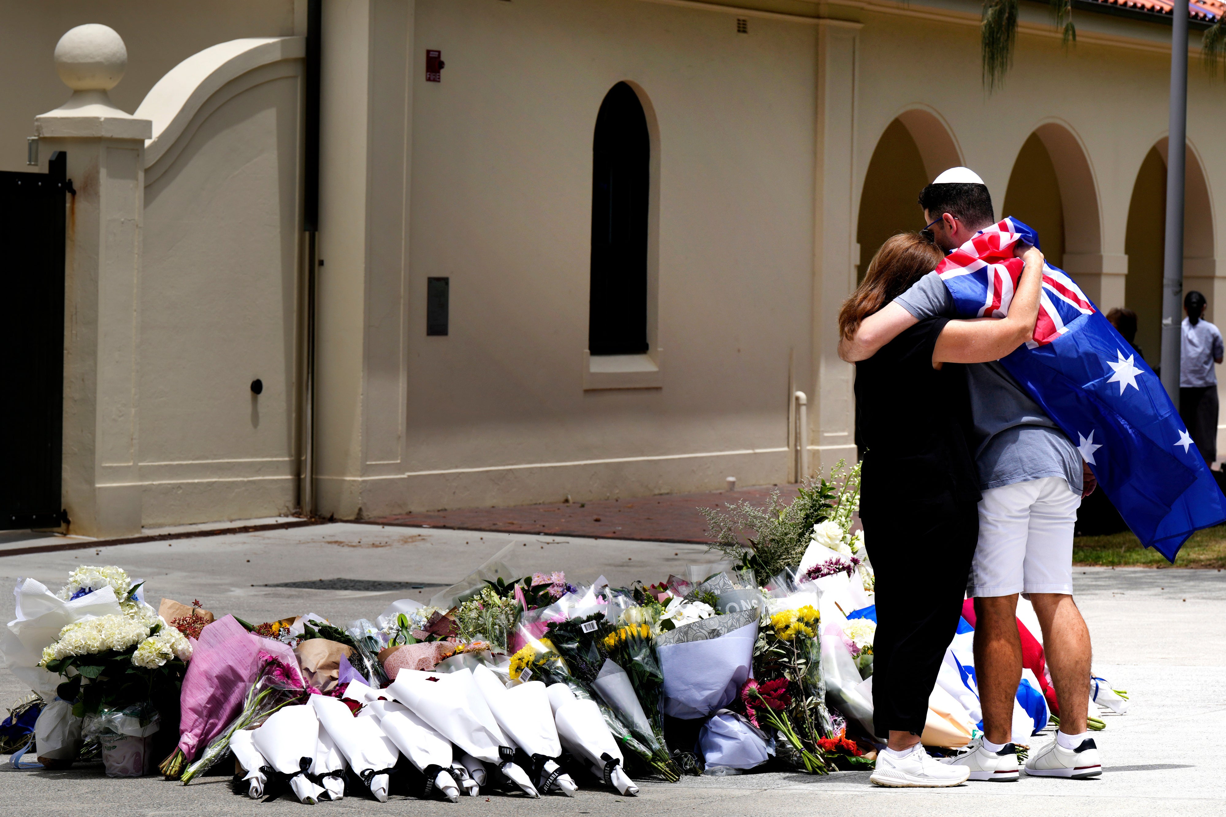 Two people stand hugging in front of flowers.
