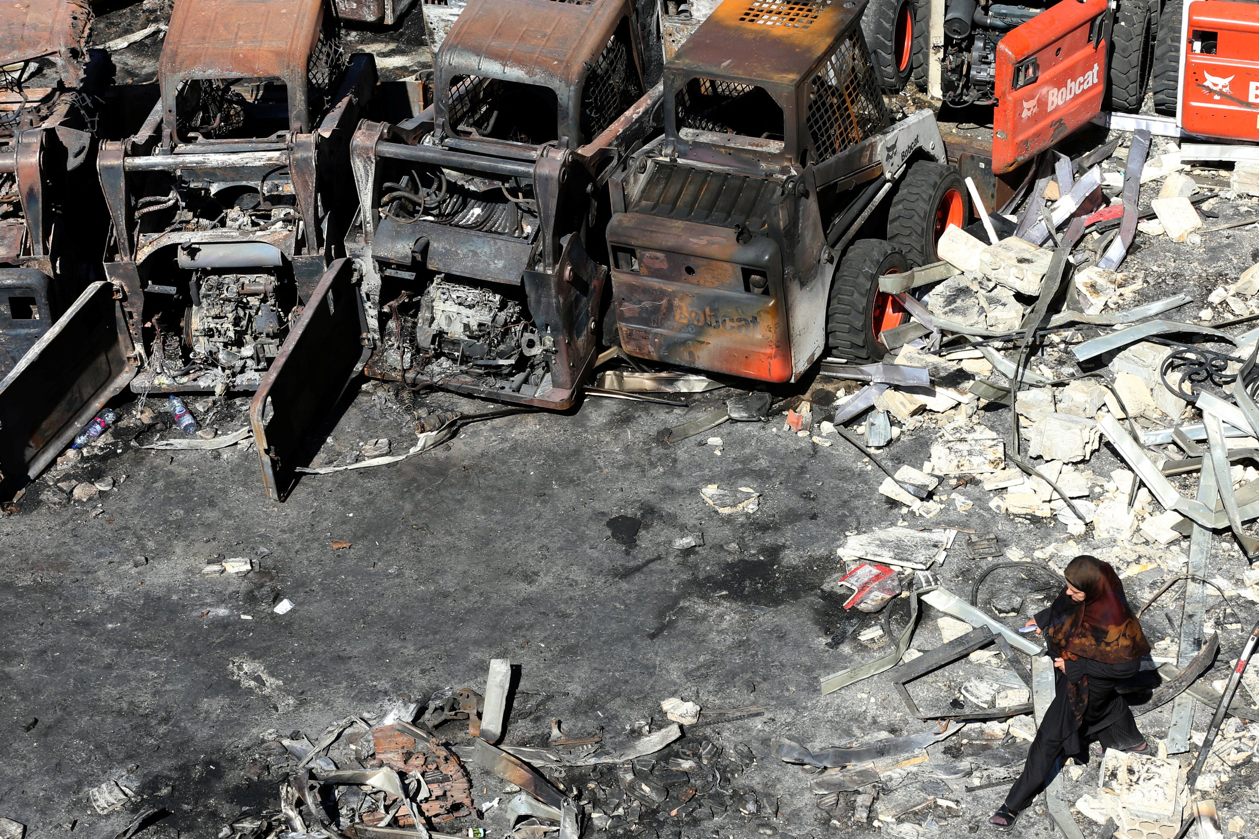 امرأة تسير أمام معدات زراعية متفحمة، في موقع غارة إسرائيلية في قرية المصيلح في جنوب لبنان، في 11 أكتوبر/تشرين الأول 2025.