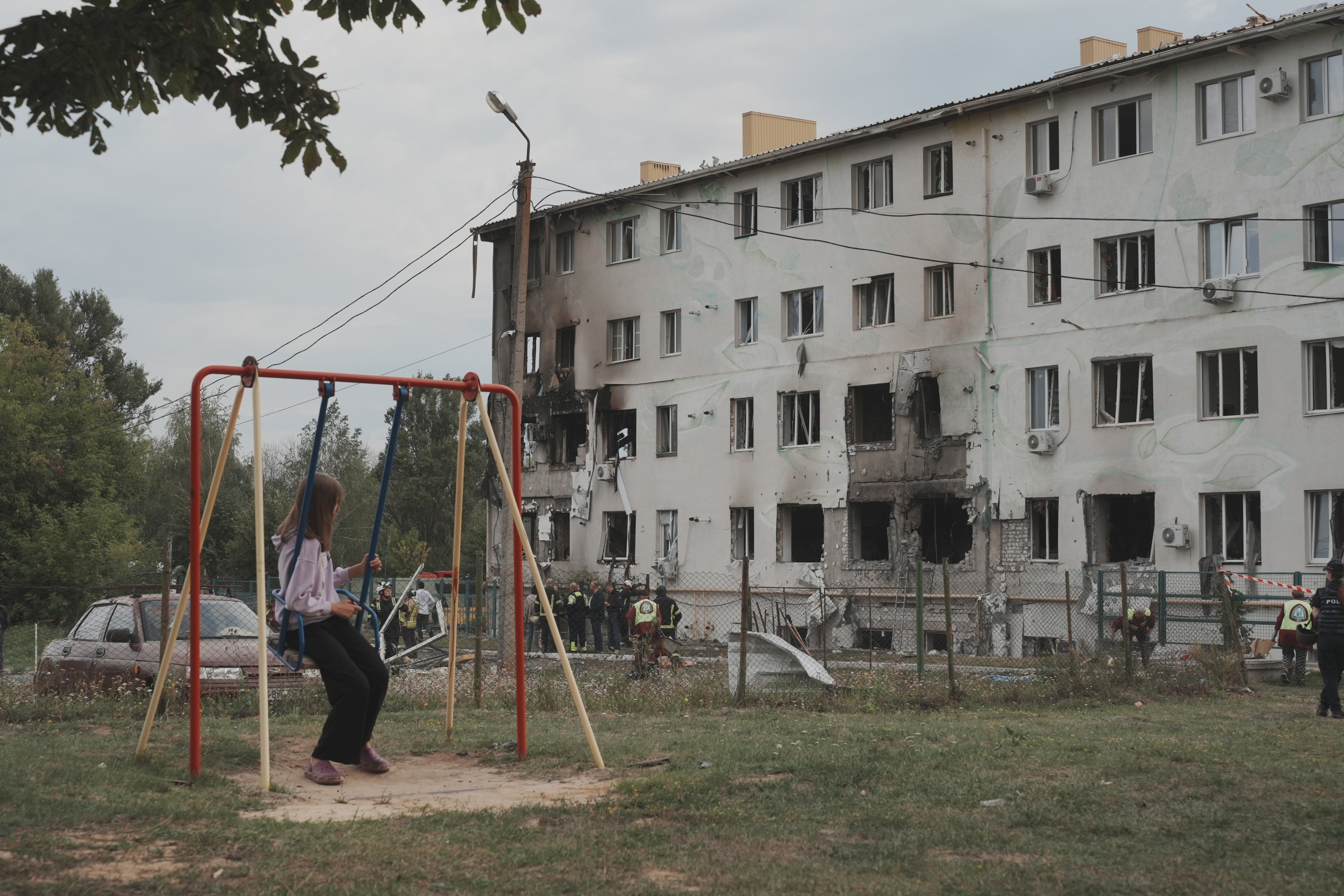 A girl on a swing looks at an apartment building in the Industrialnyi district of Kharkiv, Ukraine, damaged by a Russian drone attack that killed 7 people (including children) and injured 23, on August 18, 2025.