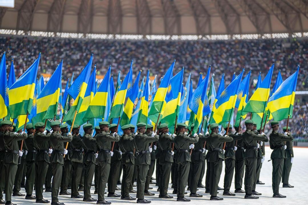Members of the Rwanda Defence Forces march while holding Rwanda flags in a stadium